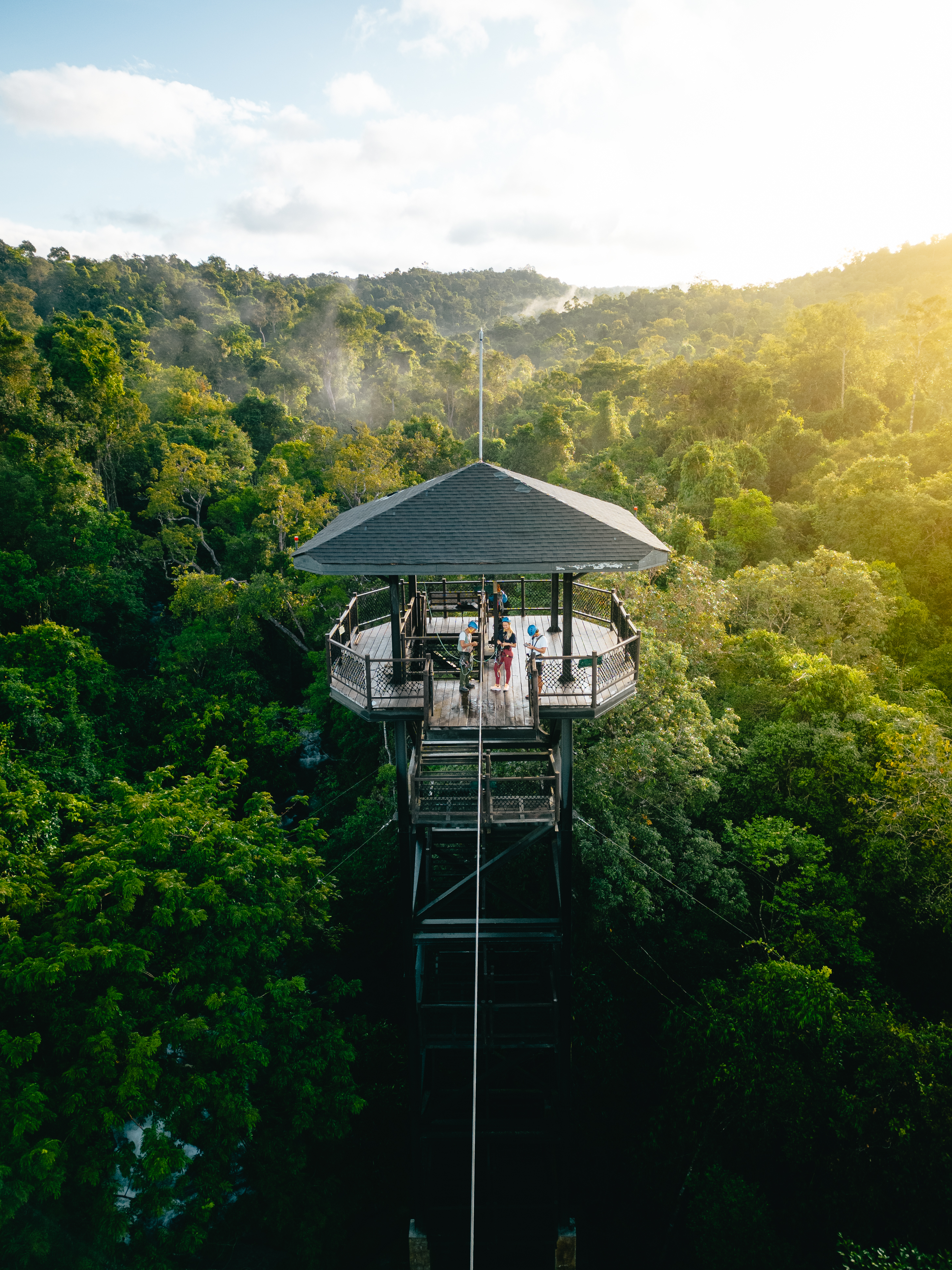 Raised lookout platform rises above dense forest with sunlight streaming through haze.