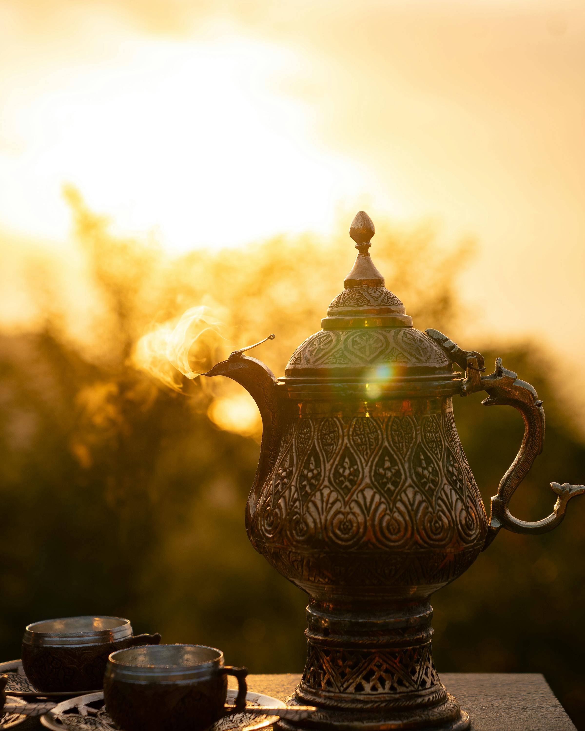 Teapot and cups sit outdoors with warm sunlight glowing in the background.