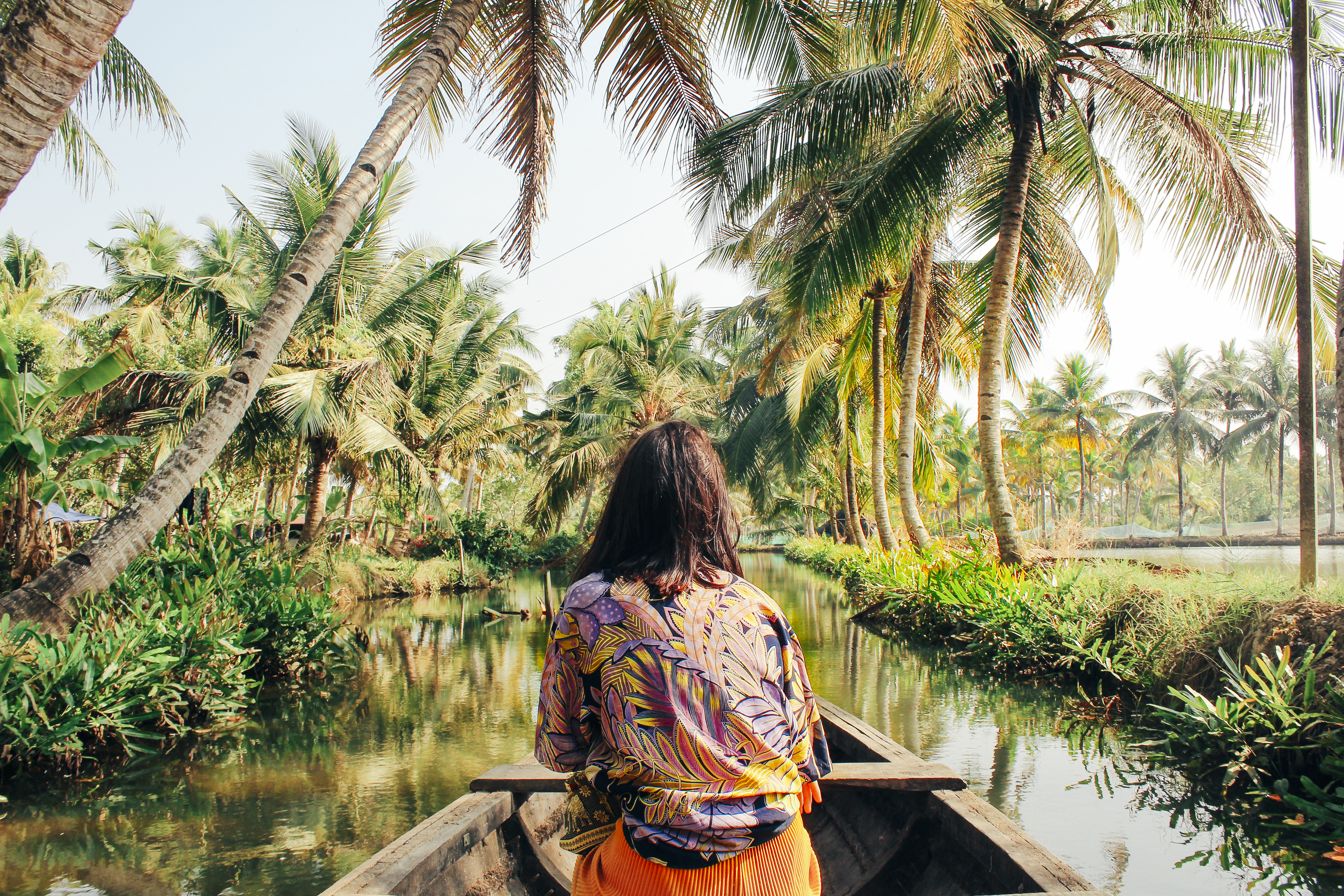 Person sits in a boat gliding along a narrow canal lined with palm trees.