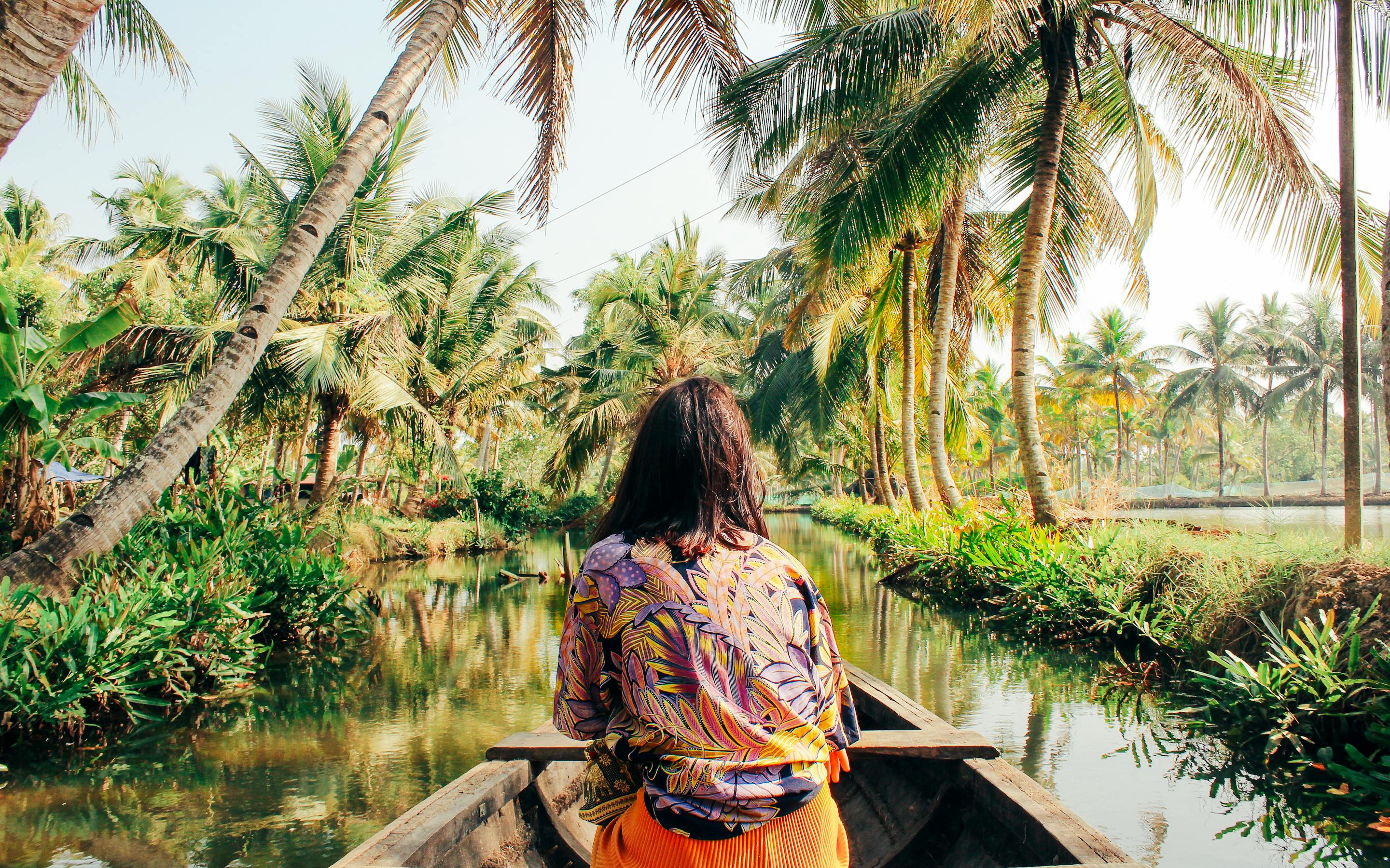 Person sits in a boat gliding along a narrow canal lined with palm trees.