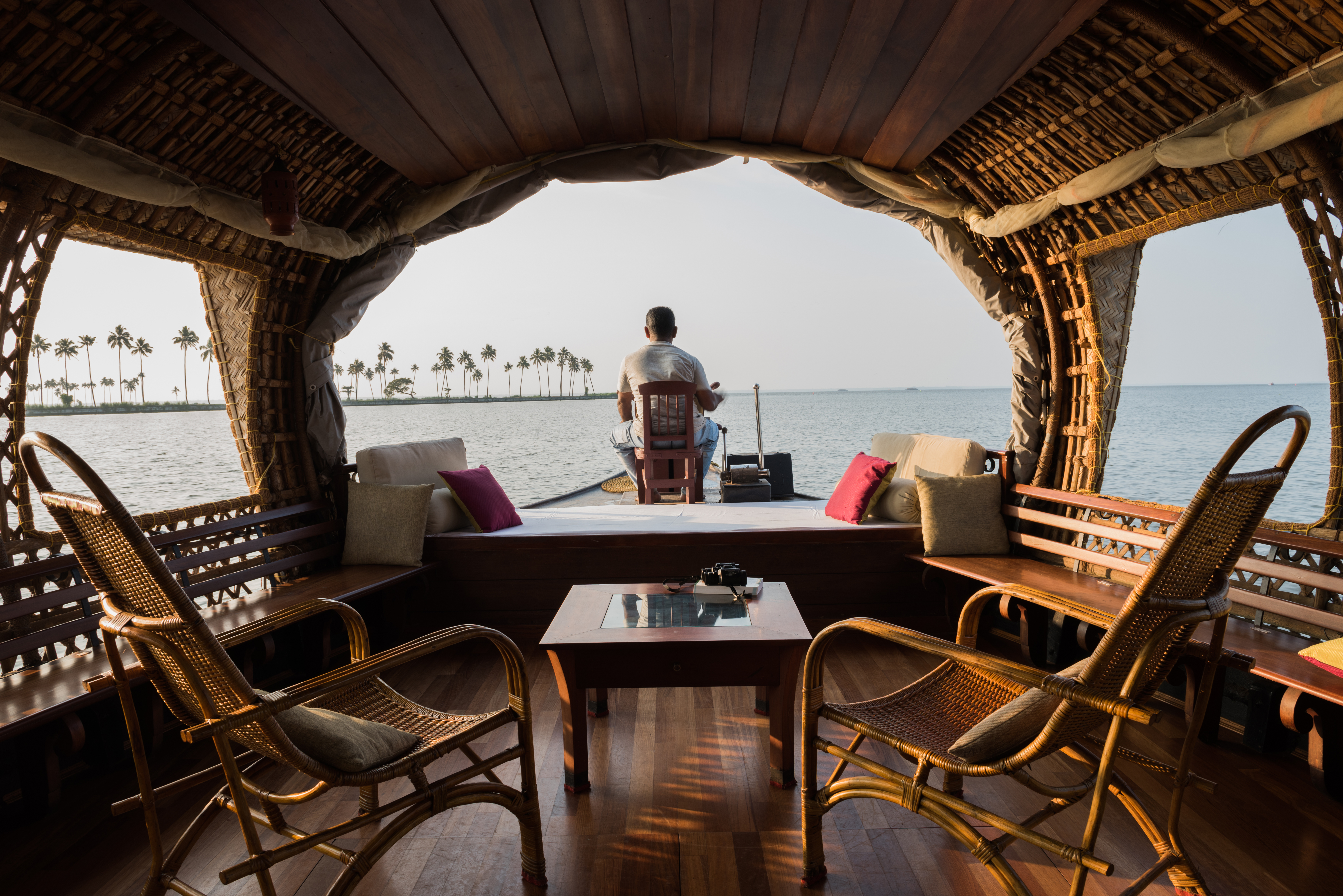Person stands at the open front of a wooden houseboat with chairs and a table.