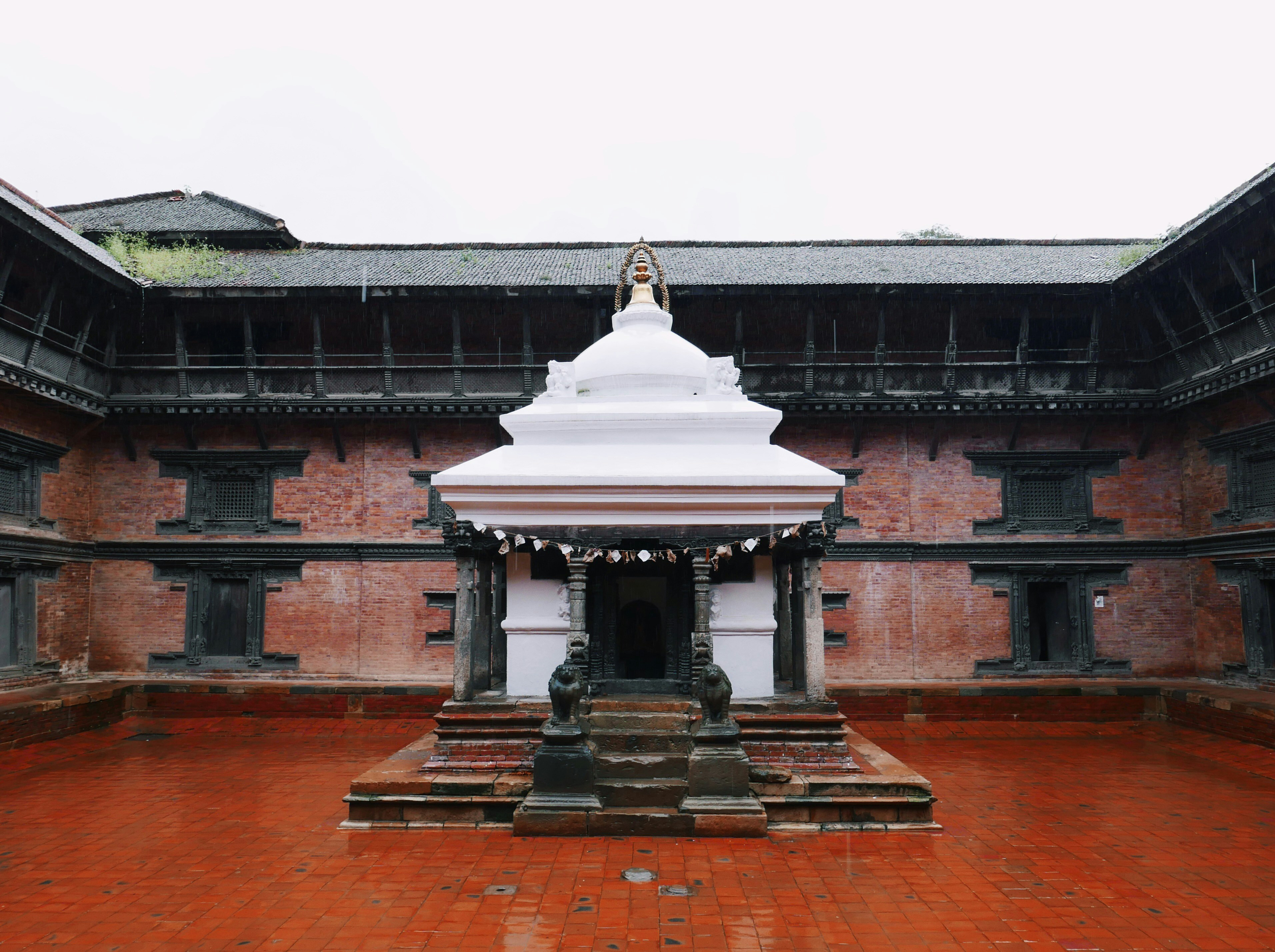Small white shrine stands in the center of a brick courtyard surrounded by dark wooden buildings.
