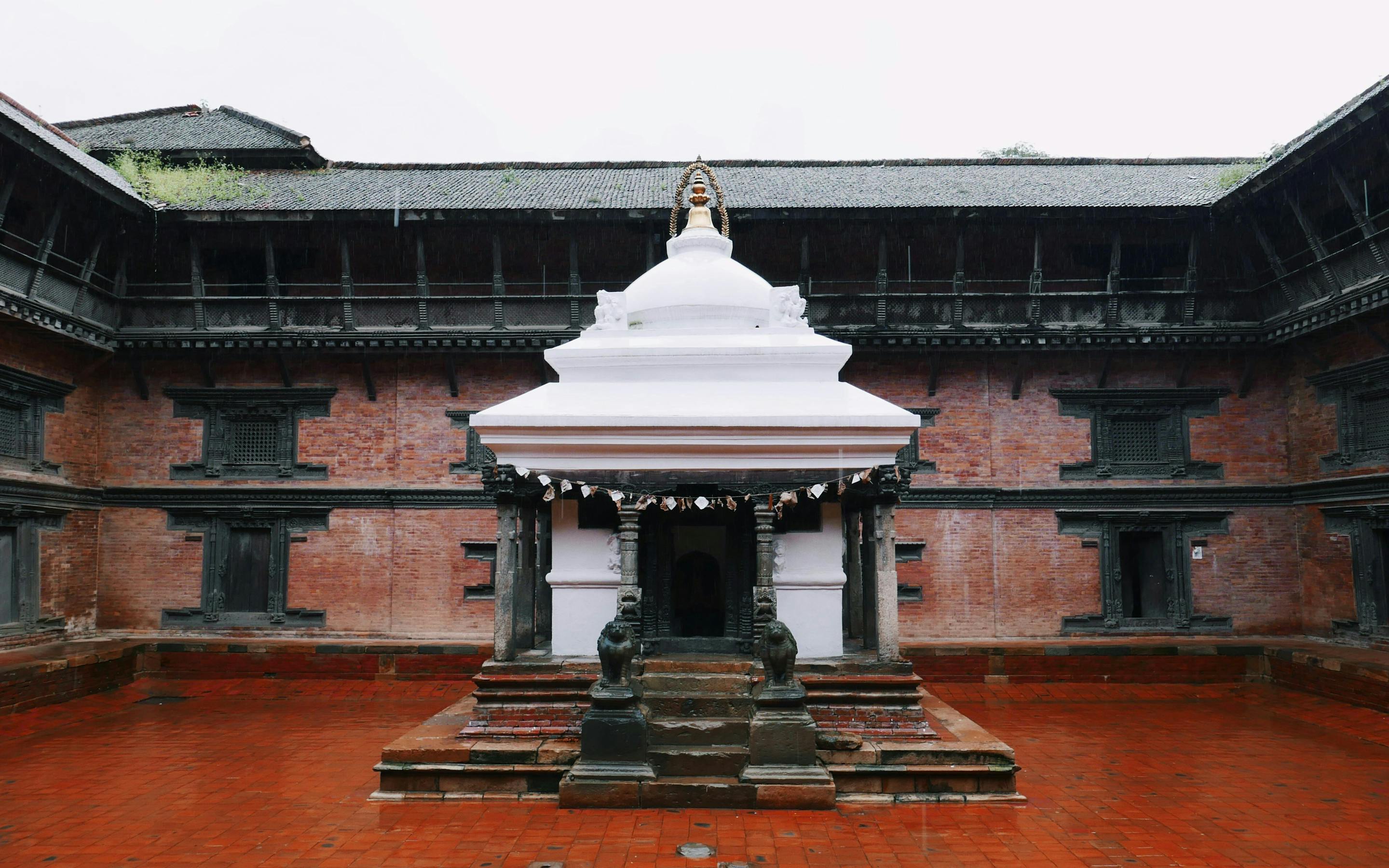 Small white shrine stands in the center of a brick courtyard surrounded by dark wooden buildings.
