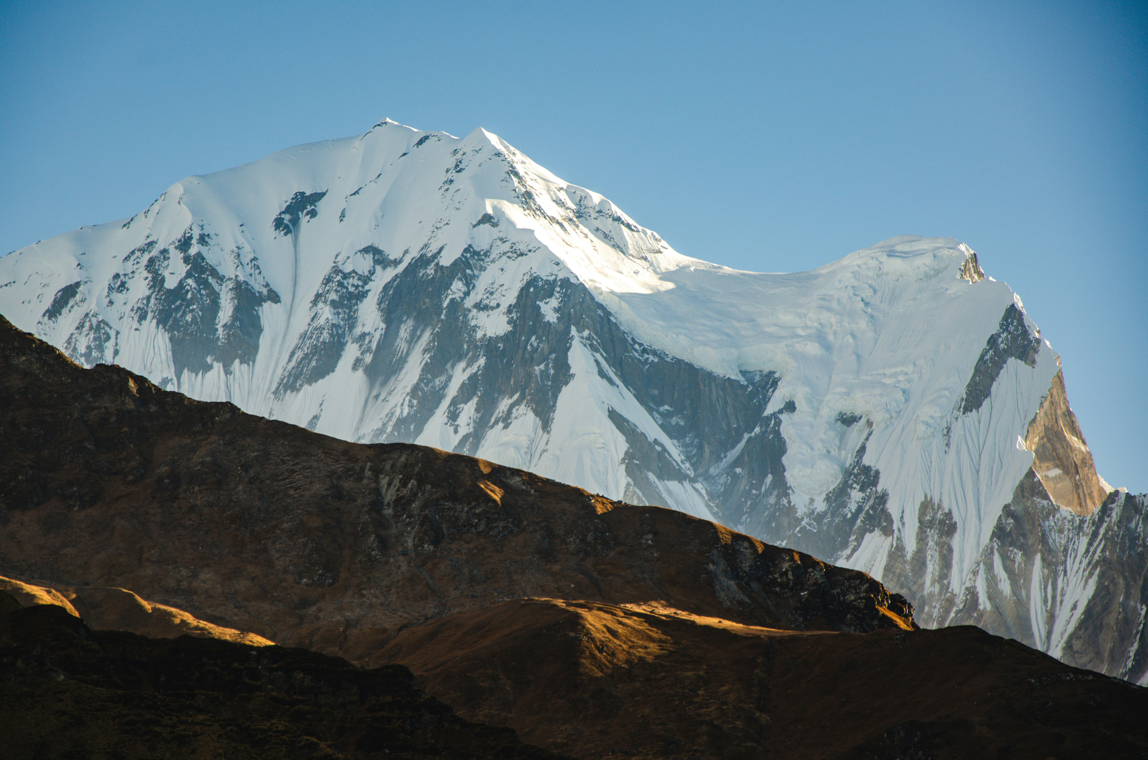 Snowy mountain peak rises above dark ridgelines under a clear blue sky.