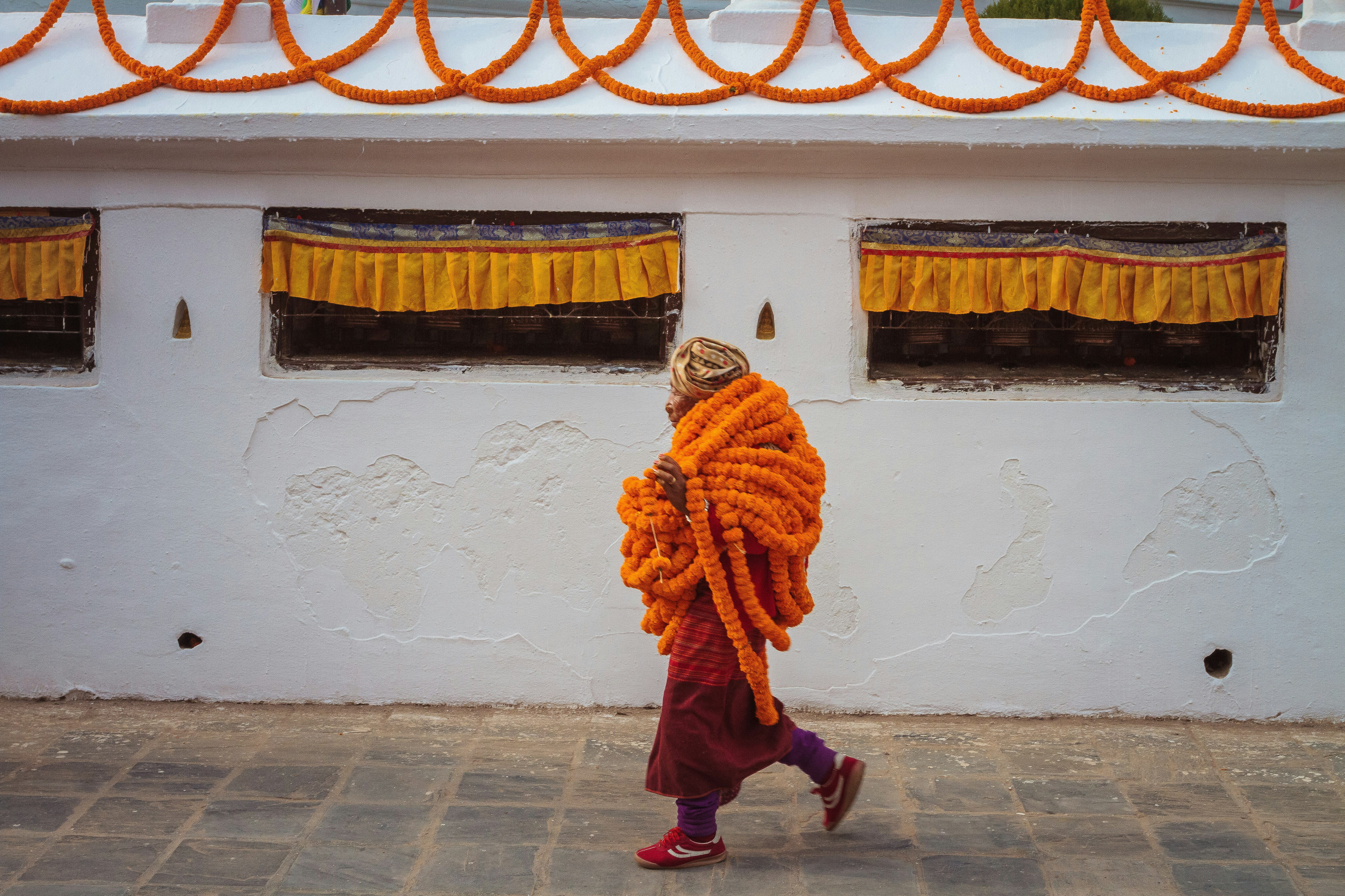 Person in orange clothing walks beside a white stupa wall on a stone path.