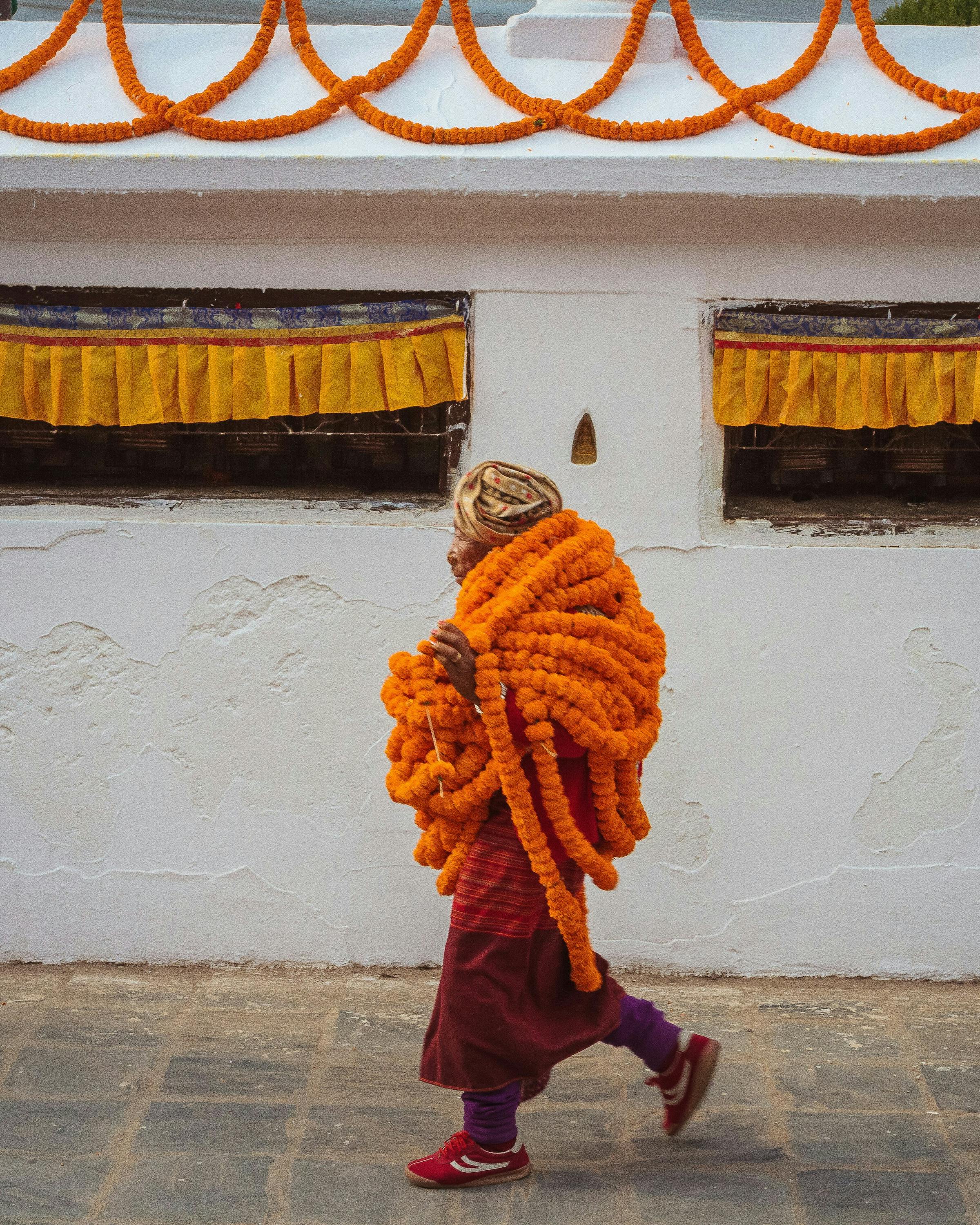 Person in orange clothing walks beside a white stupa wall on a stone path.
