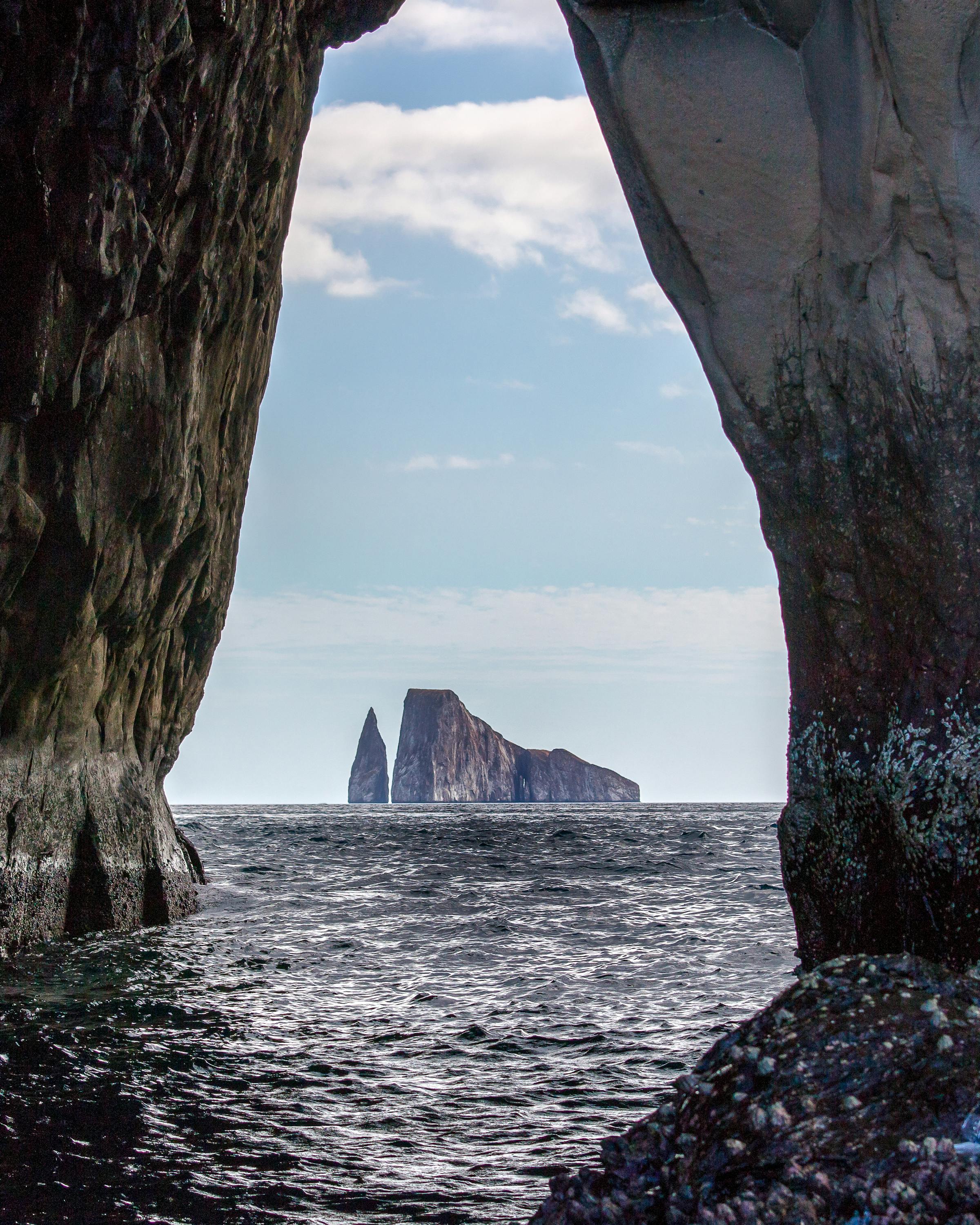 View from inside a sea cave frames ocean water and a rocky islet in the distance.