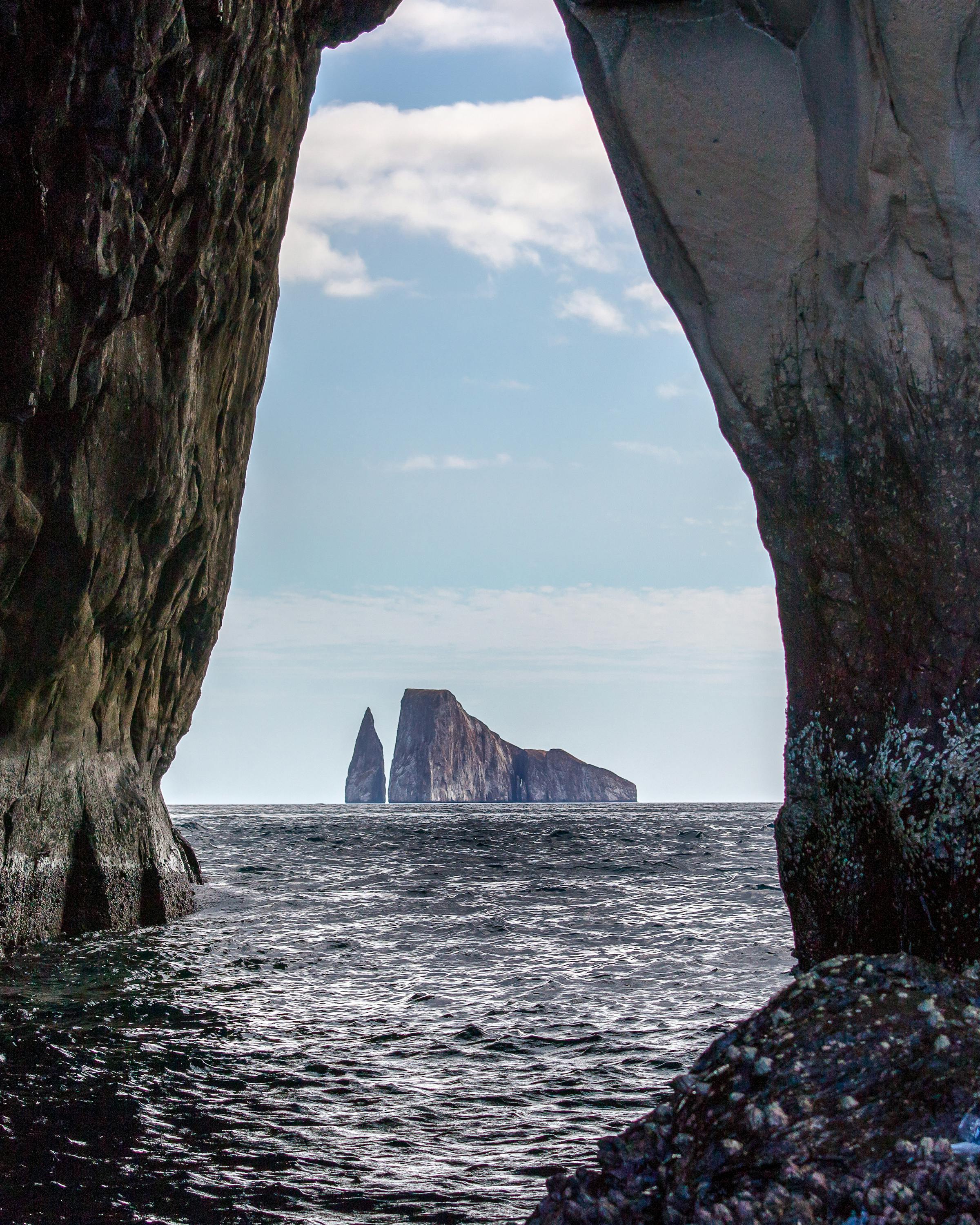 View from inside a sea cave frames ocean water and a rocky islet in the distance.