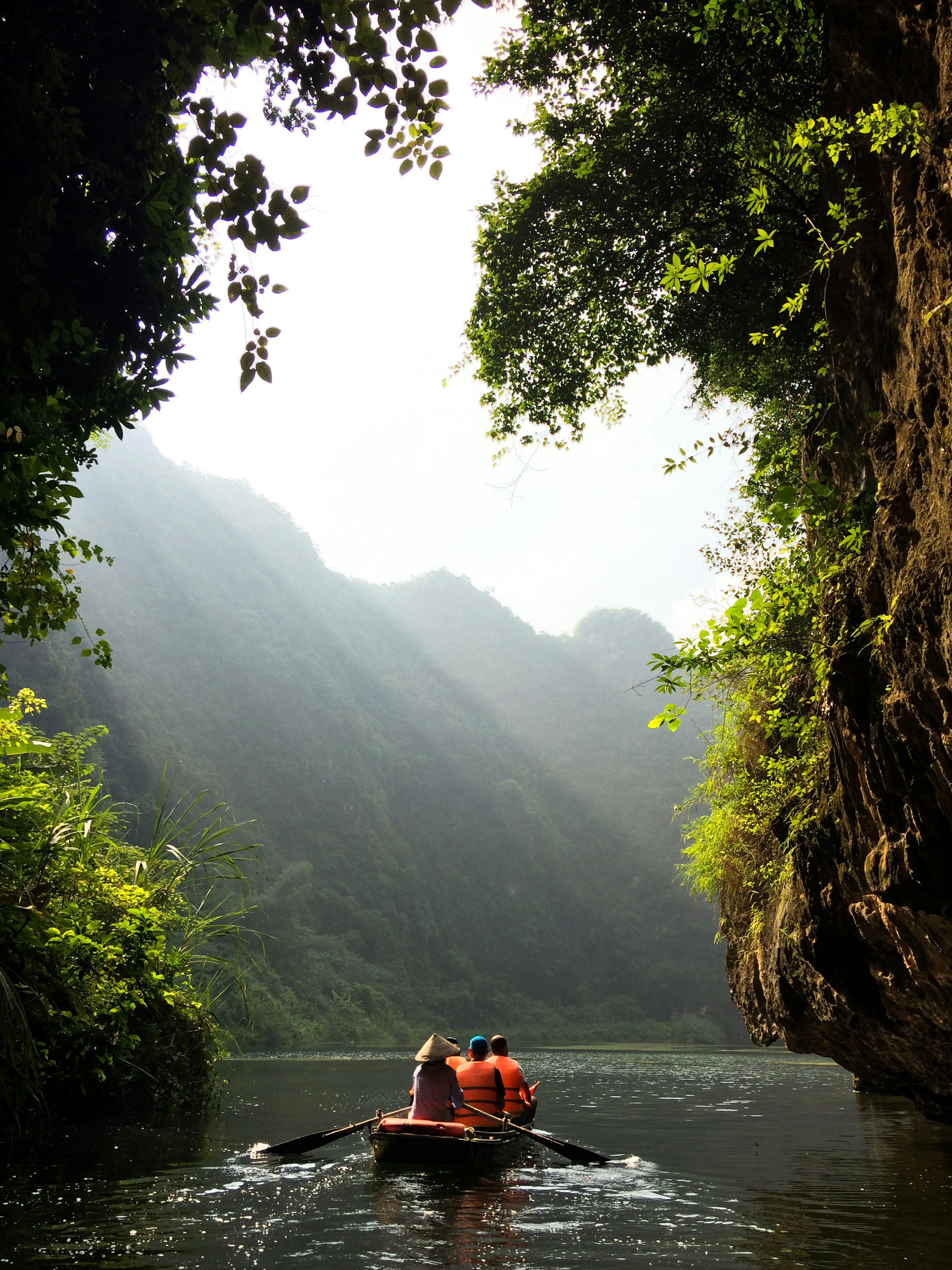 Small boat glides through a narrow river canyon with steep cliffs and sunbeams.