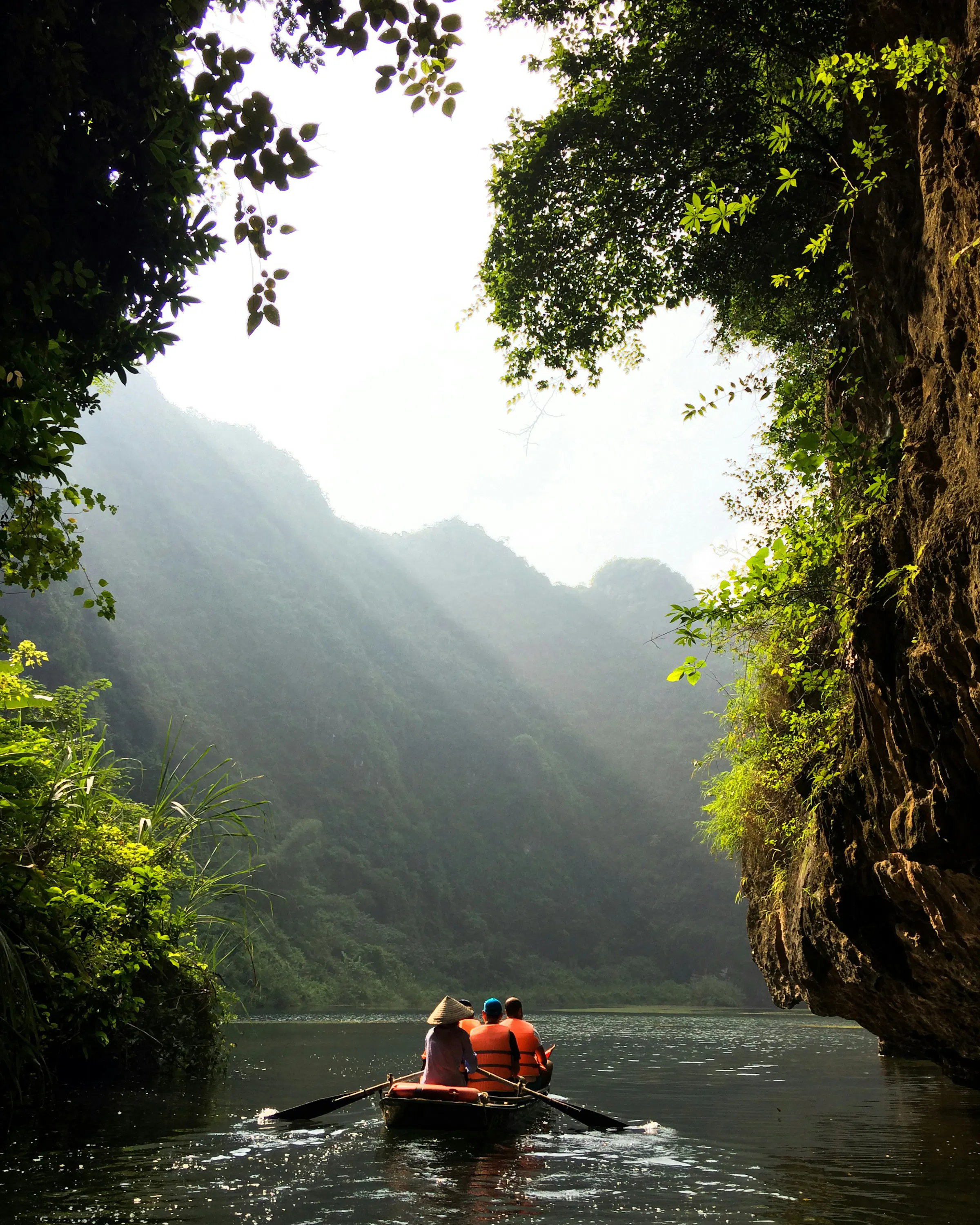 Small boat glides through a narrow river canyon with steep cliffs and sunbeams.