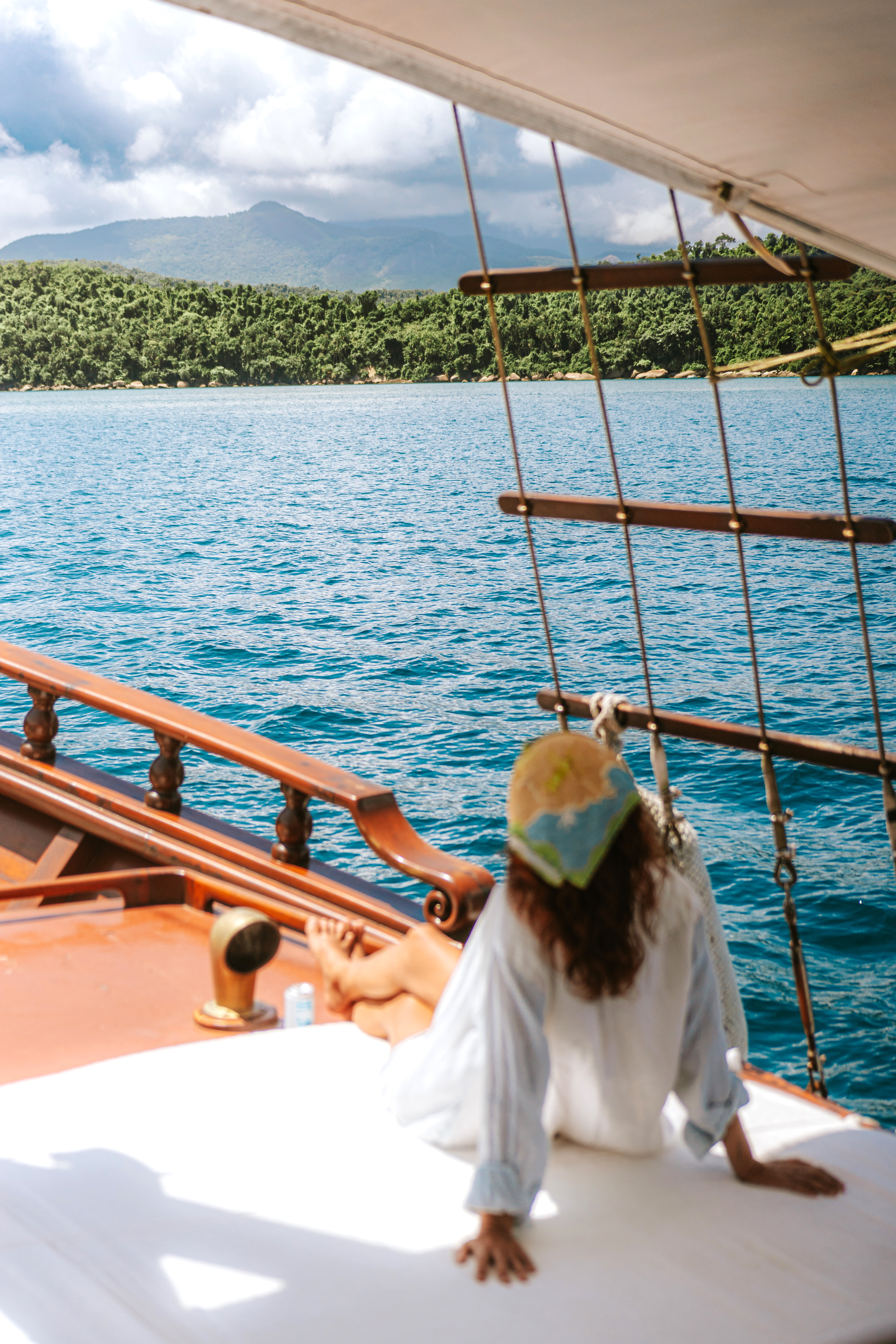 Person relaxes on a boat deck overlooking bright blue water and a distant coastline.