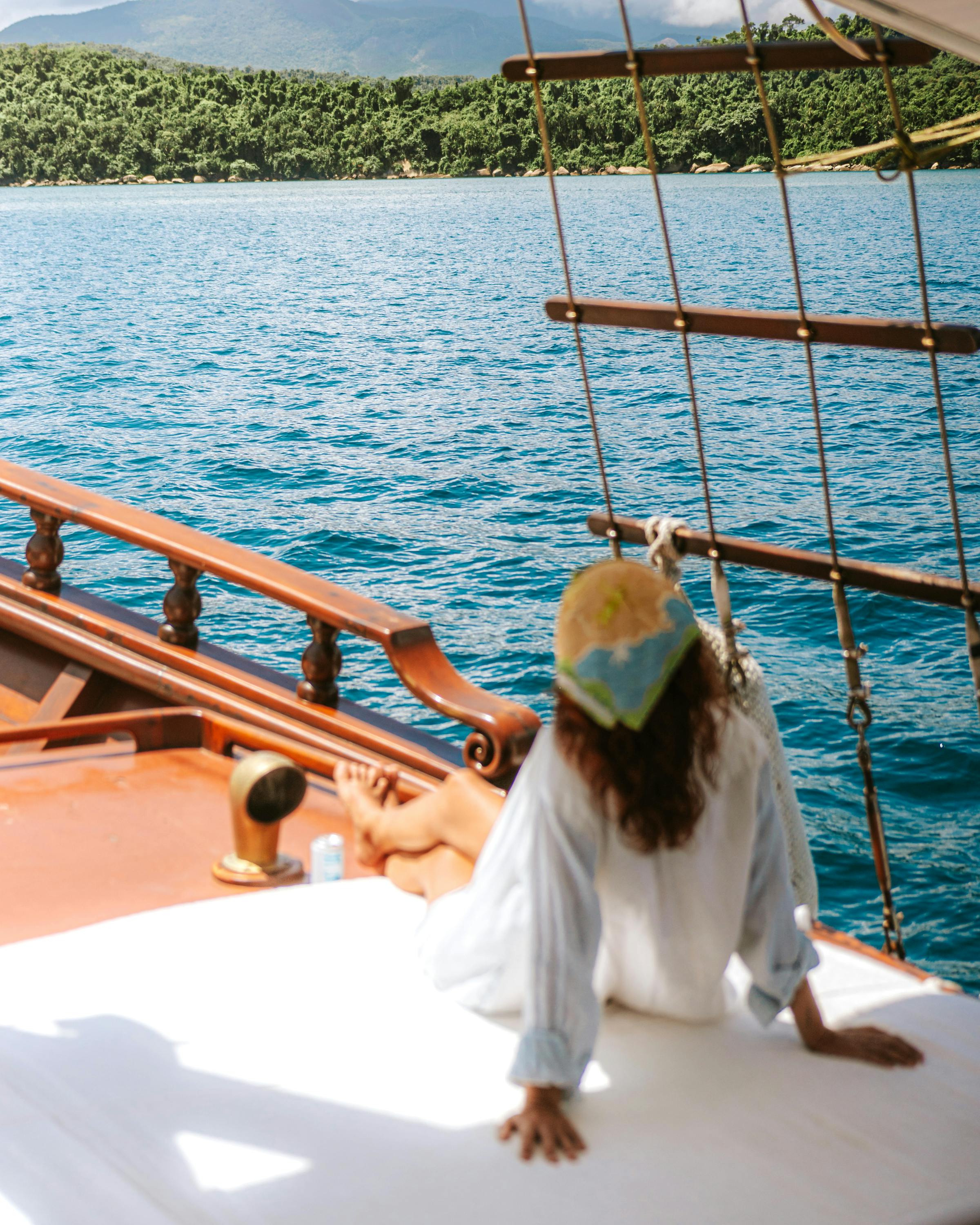 Person relaxes on a boat deck overlooking bright blue water and a distant coastline.