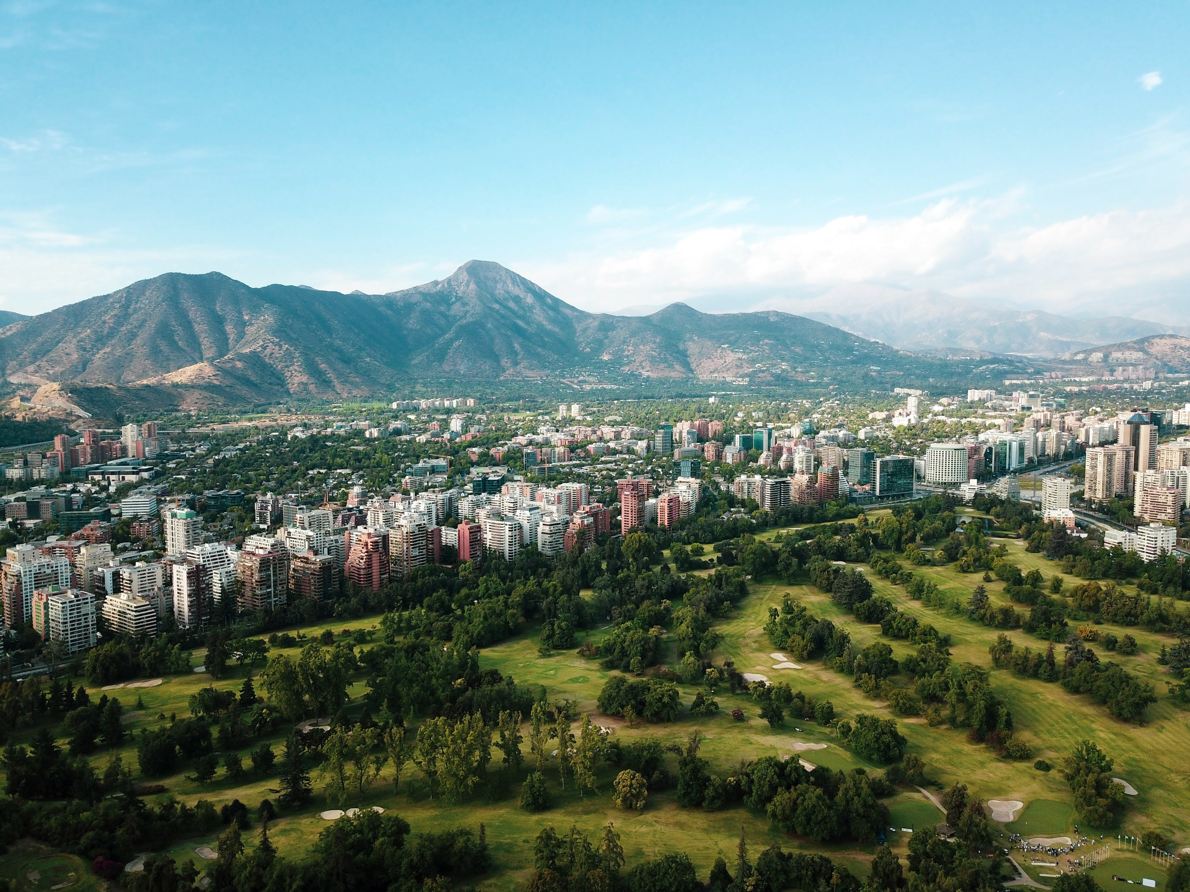 Aerial view of a city with a large green park and mountains in the distance.