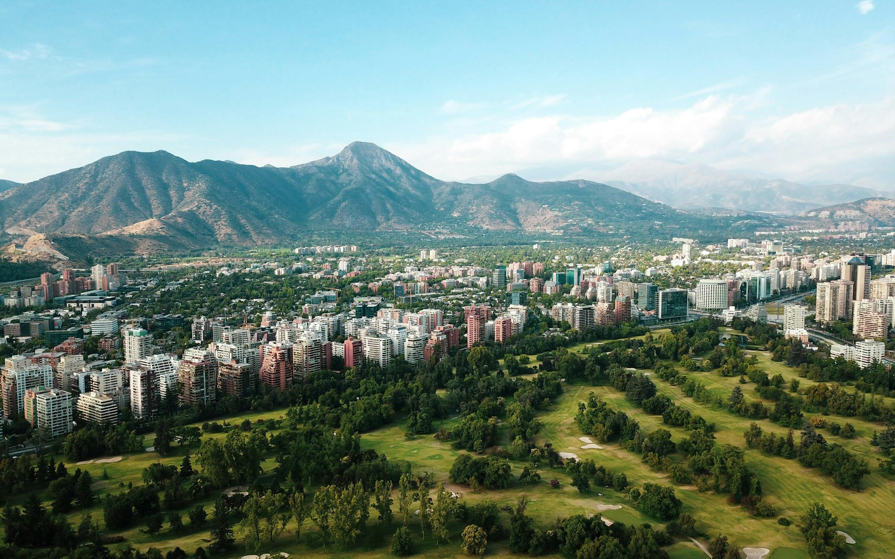 Aerial view of a city with a large green park and mountains in the distance.