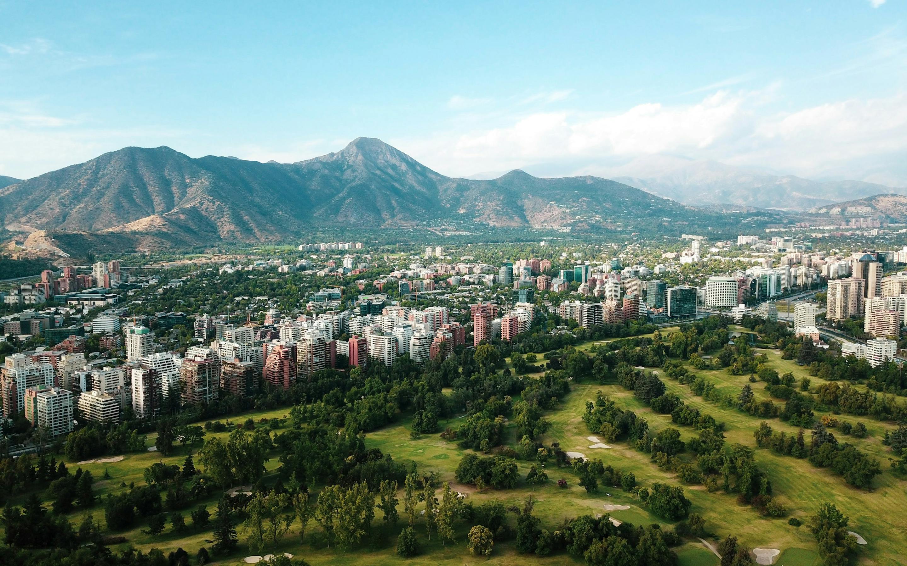 Aerial view of a city with a large green park and mountains in the distance.