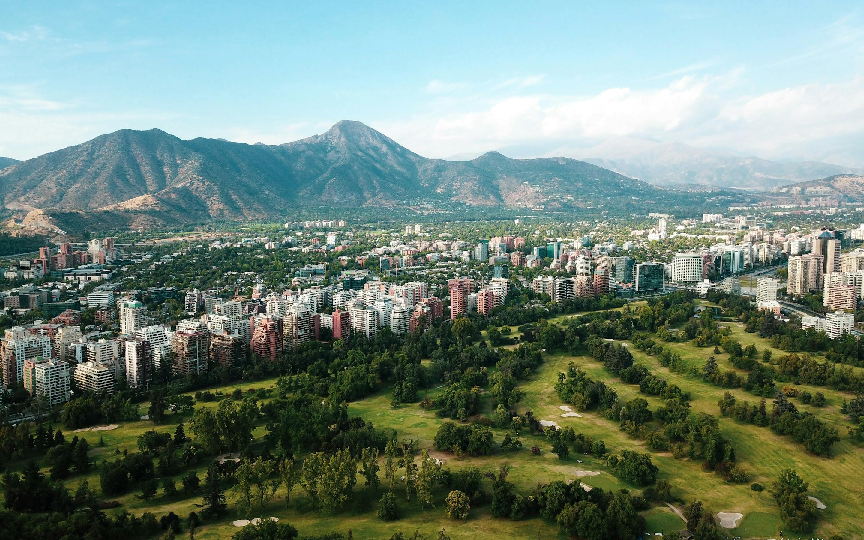 Aerial view of a city with a large green park and mountains in the distance.