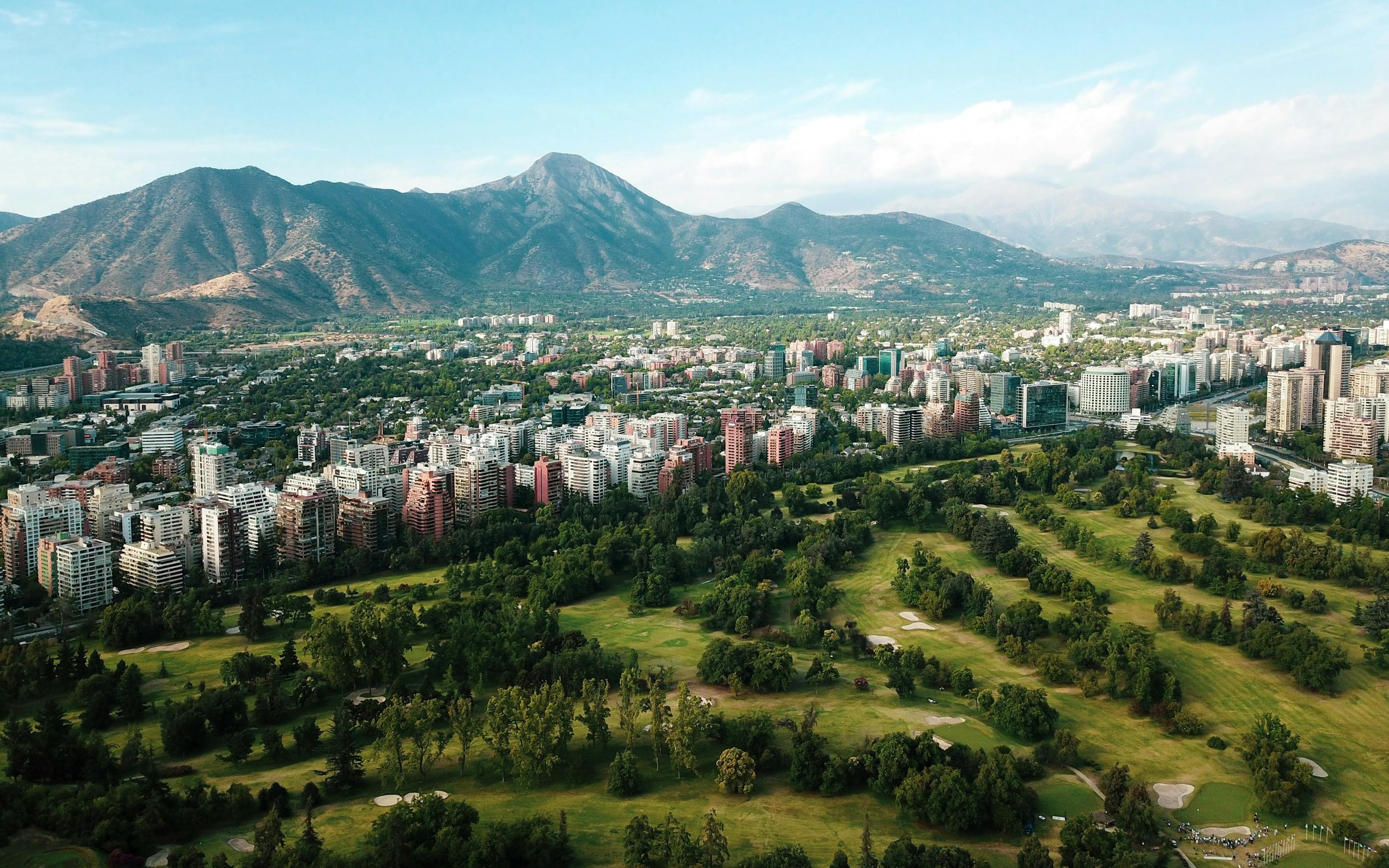 Aerial view of a city with a large green park and mountains in the distance.
