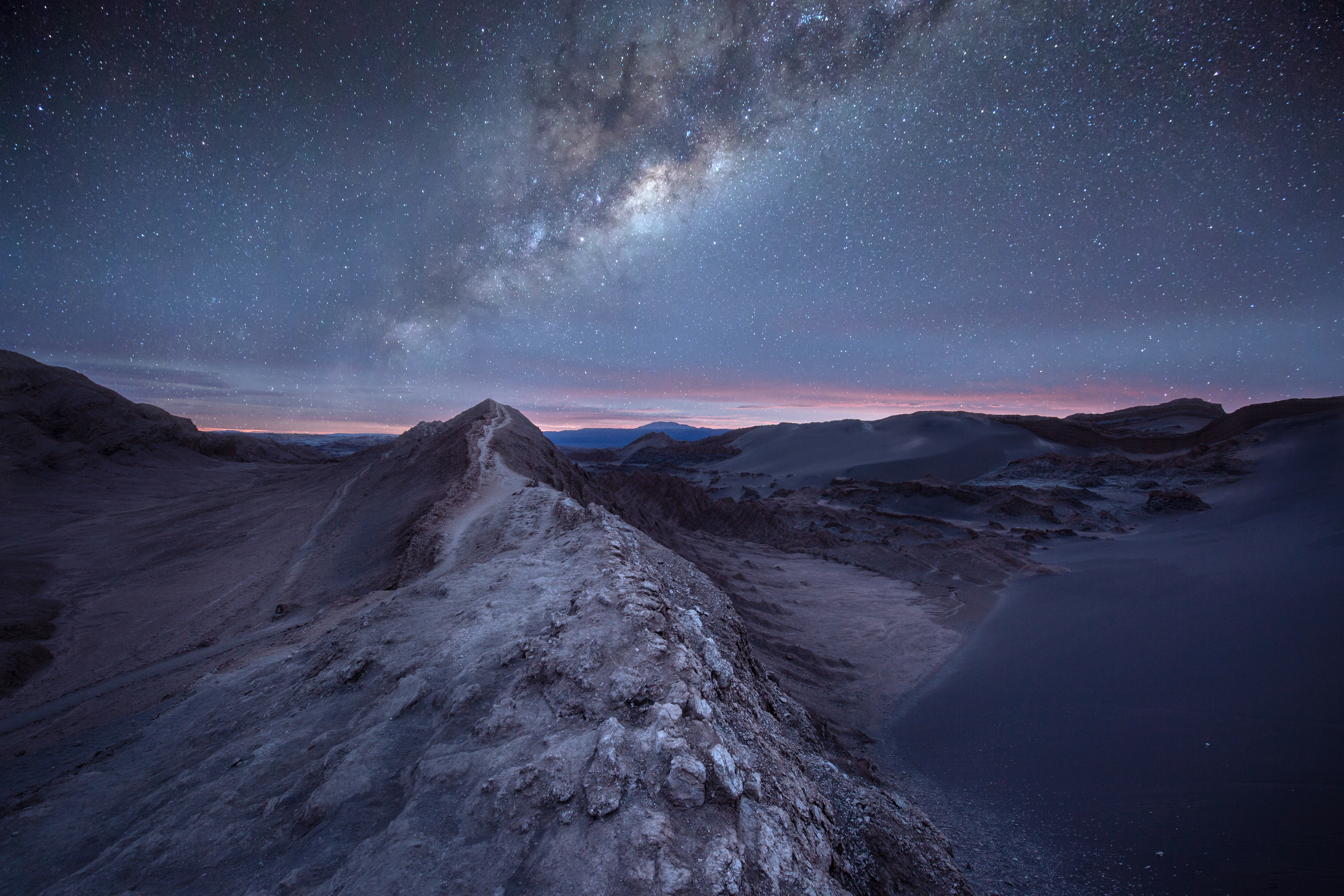 Milky Way arches over desert dunes under a dark night sky.