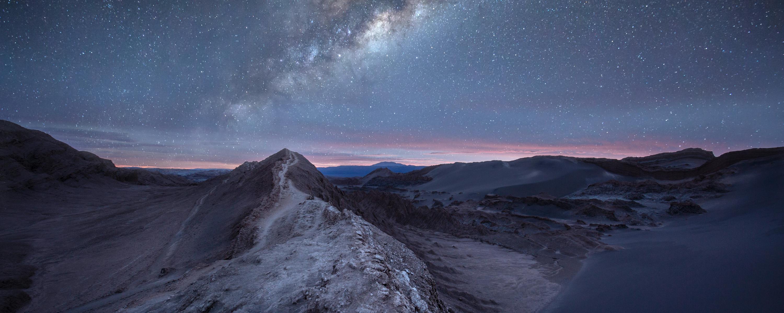 Milky Way arches over desert dunes under a dark night sky.