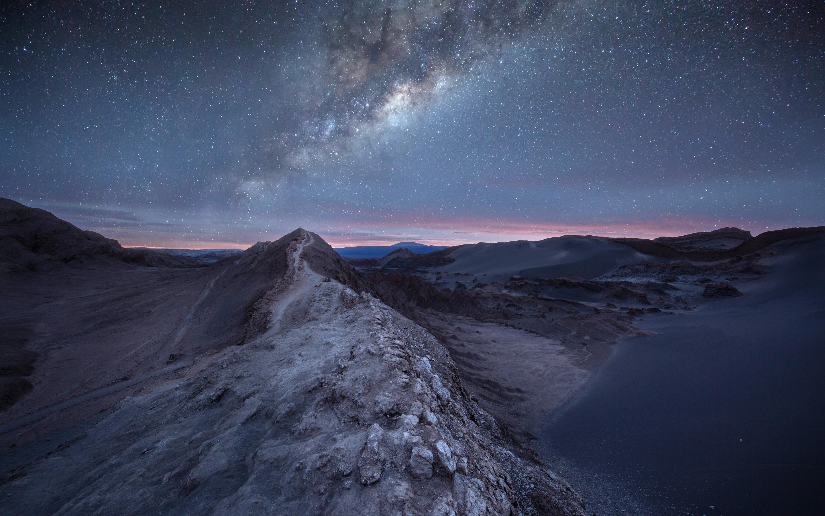 Milky Way arches over desert dunes under a dark night sky.