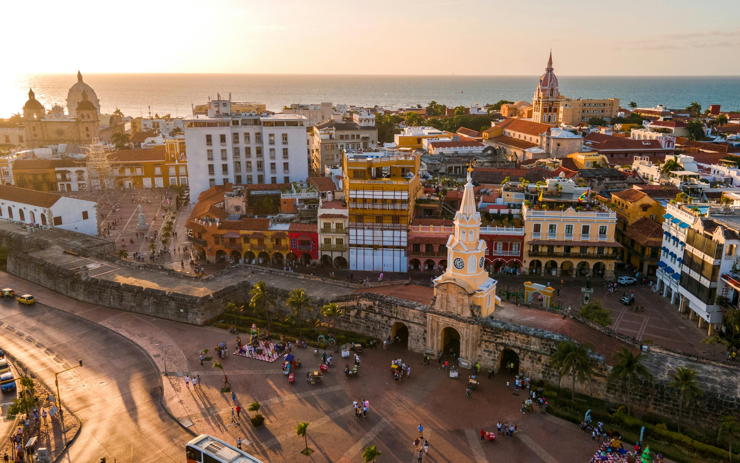 Aerial view of a historic city center with plazas and rooftops in warm evening light.