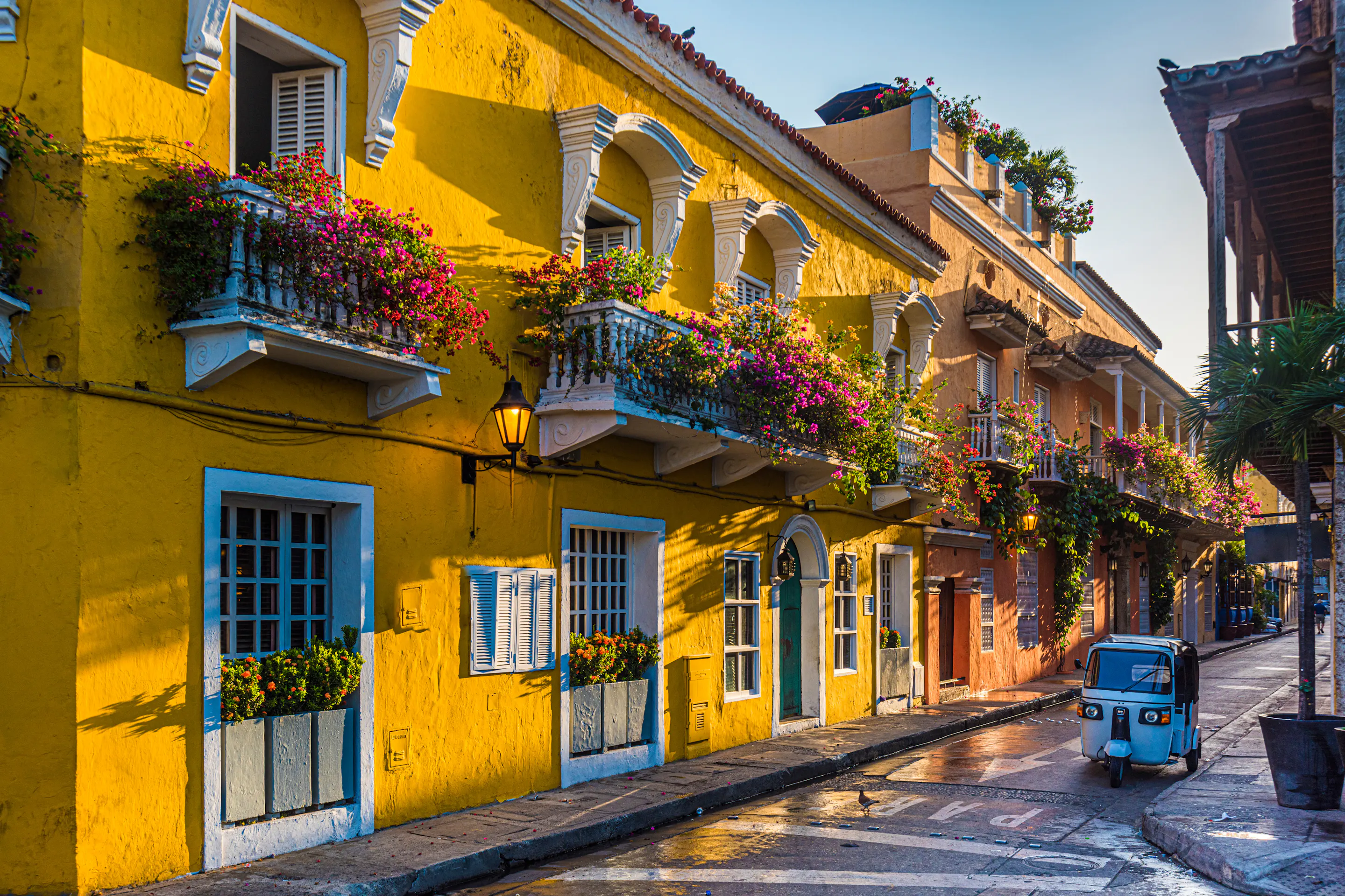 Yellow colonial street with flowered balconies and a small car parked along the curb.