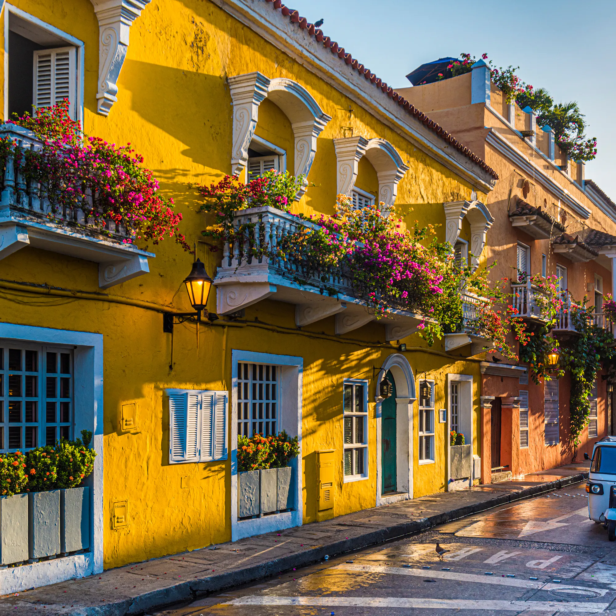 Yellow colonial street with flowered balconies and a small car parked along the curb.