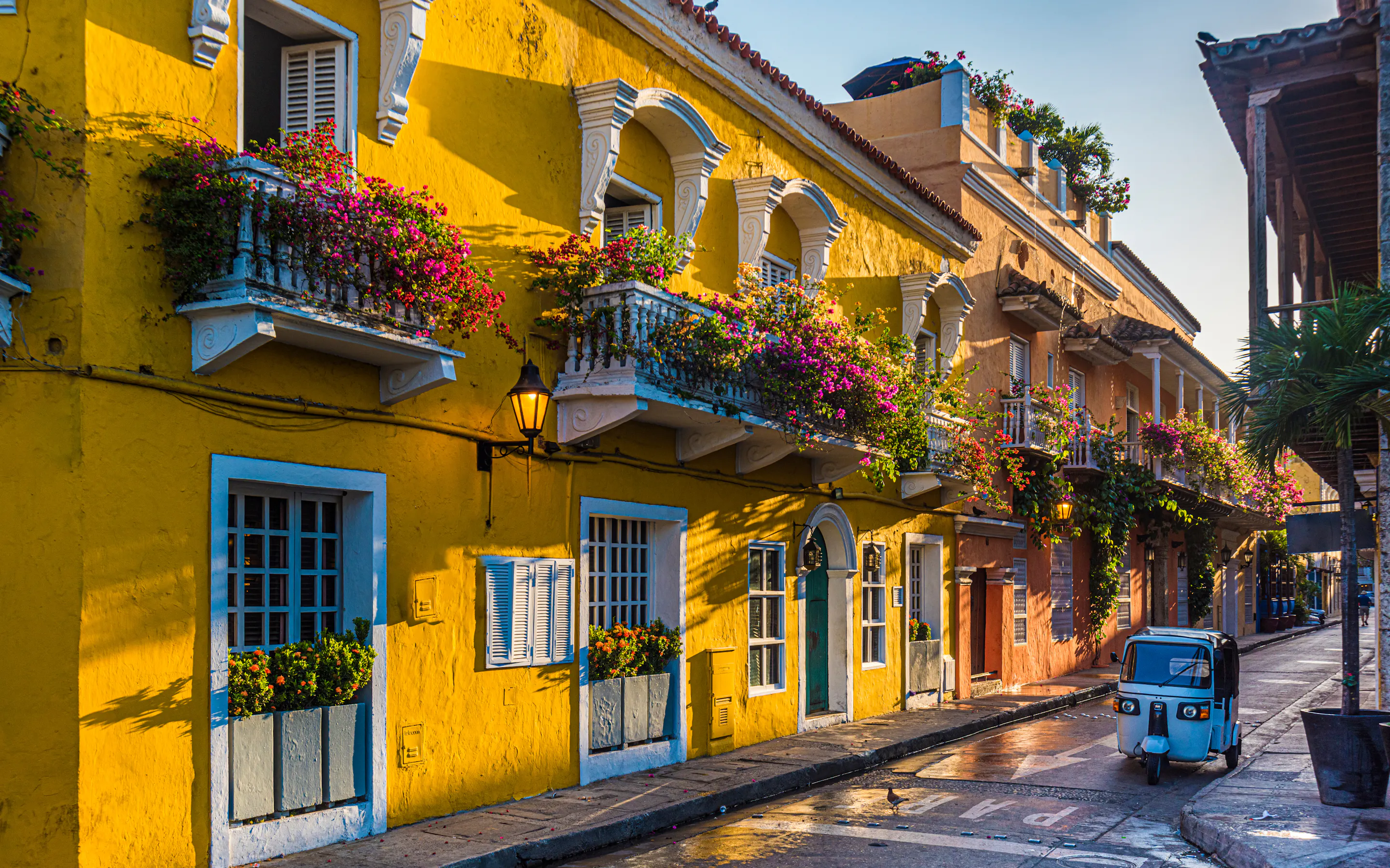 Yellow colonial street with flowered balconies and a small car parked along the curb.