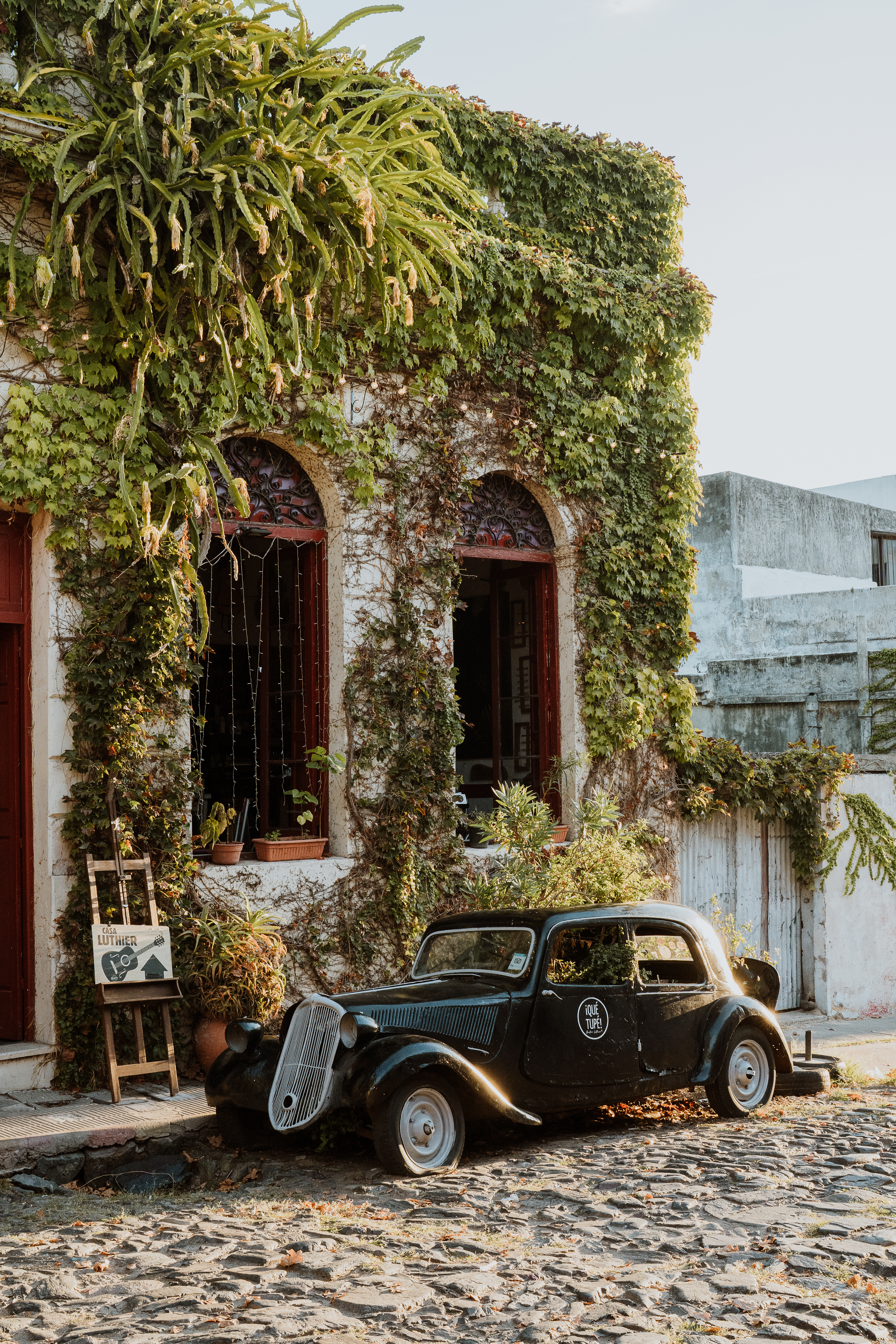 Vintage car parked beside an ivy-covered building on a quiet cobblestone street.