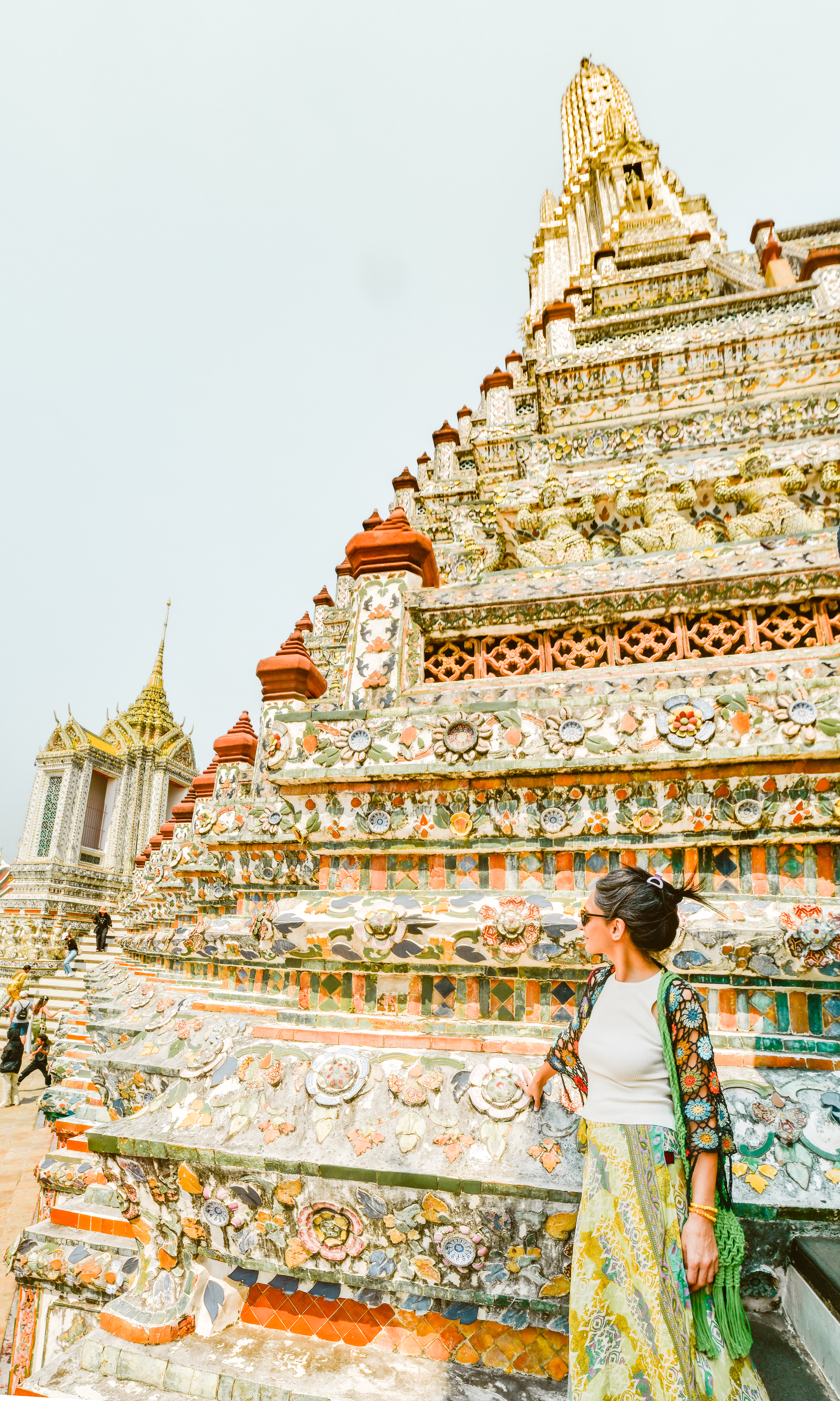 Traveler climbs ornate temple steps covered in patterned tiles, with a spire rising above in bright sun under soft daylight.