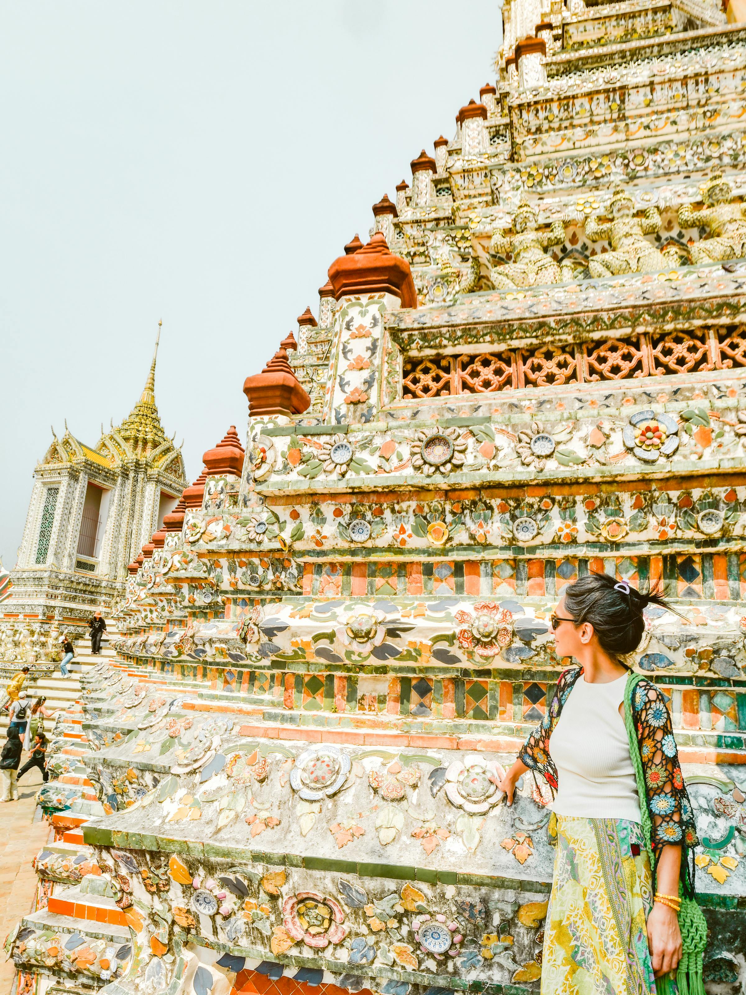 Traveler climbs ornate temple steps covered in patterned tiles, with a spire rising above in bright sun under soft daylight.