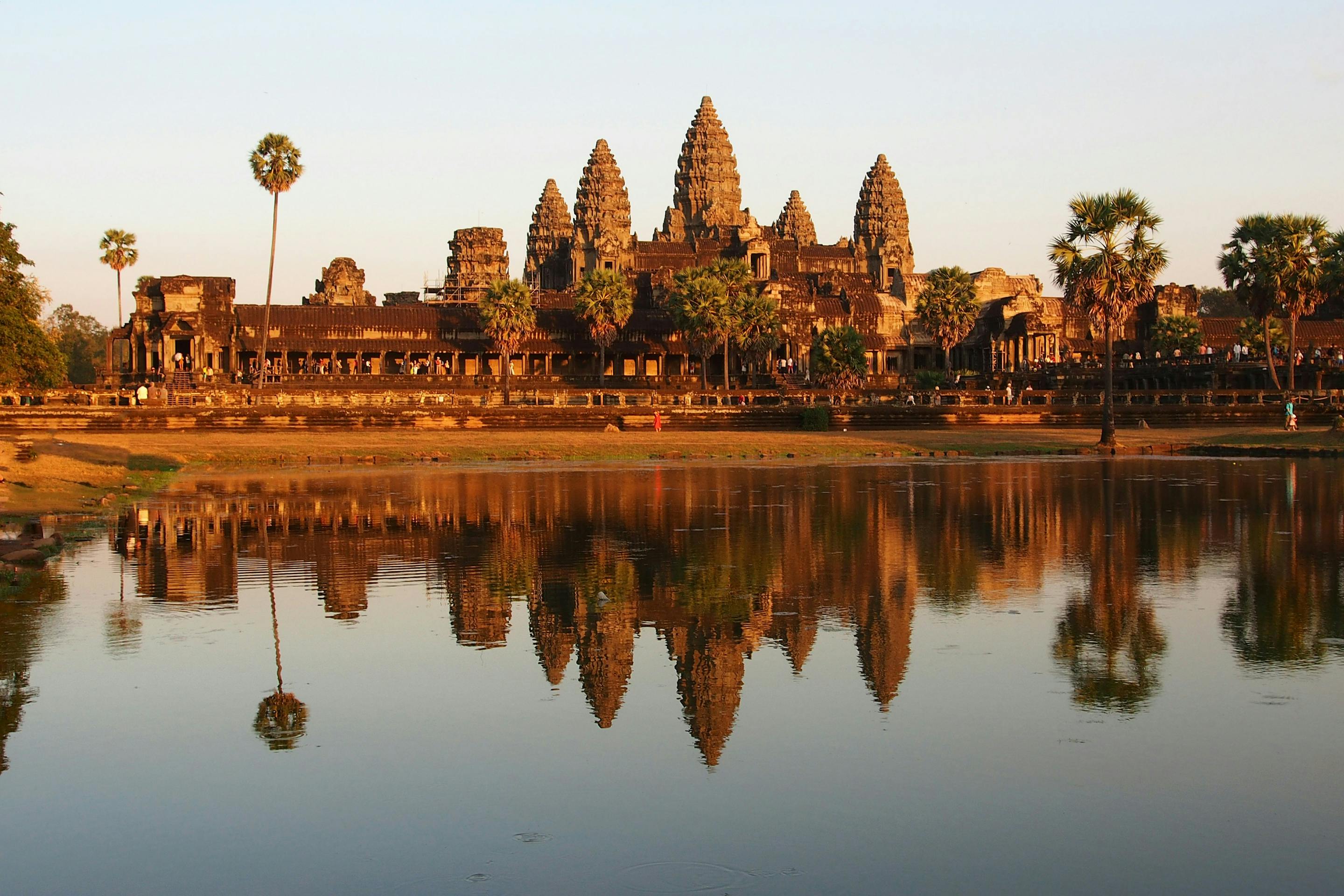 Temple towers reflect in still water at sunrise, with warm light and symmetrical shapes across the pond.
