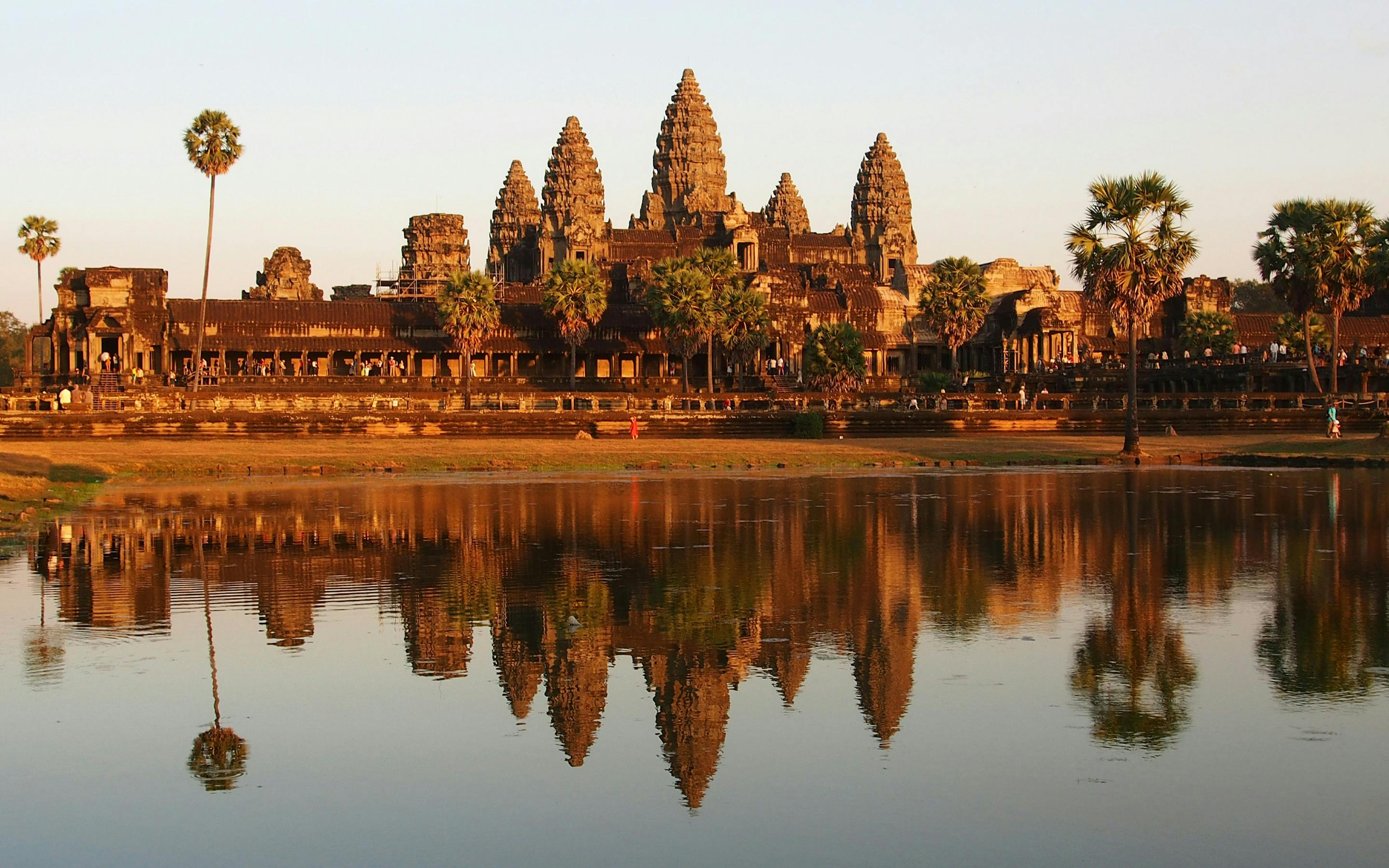 Temple towers reflect in still water at sunrise, with warm light and symmetrical shapes across the pond.