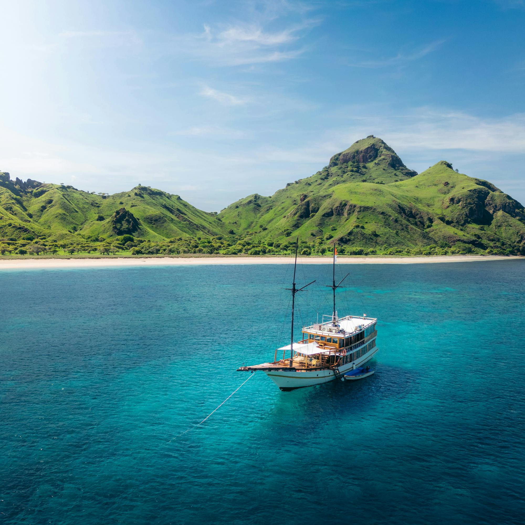Small boat floats in a turquoise bay, with rugged hills and clear water.