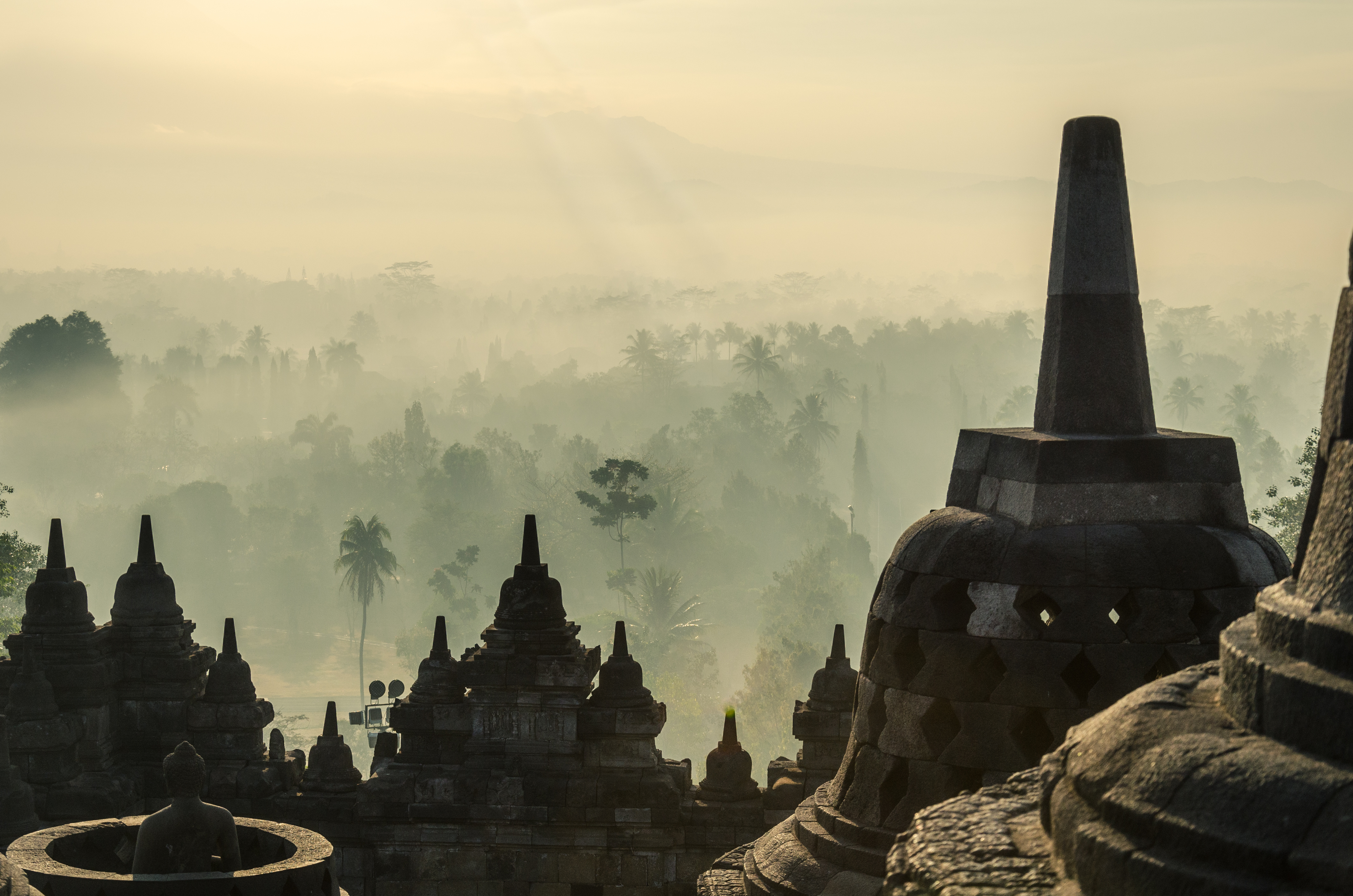 Temple stupas rise above morning fog, with a soft sunrise and layered silhouettes across the skyline.