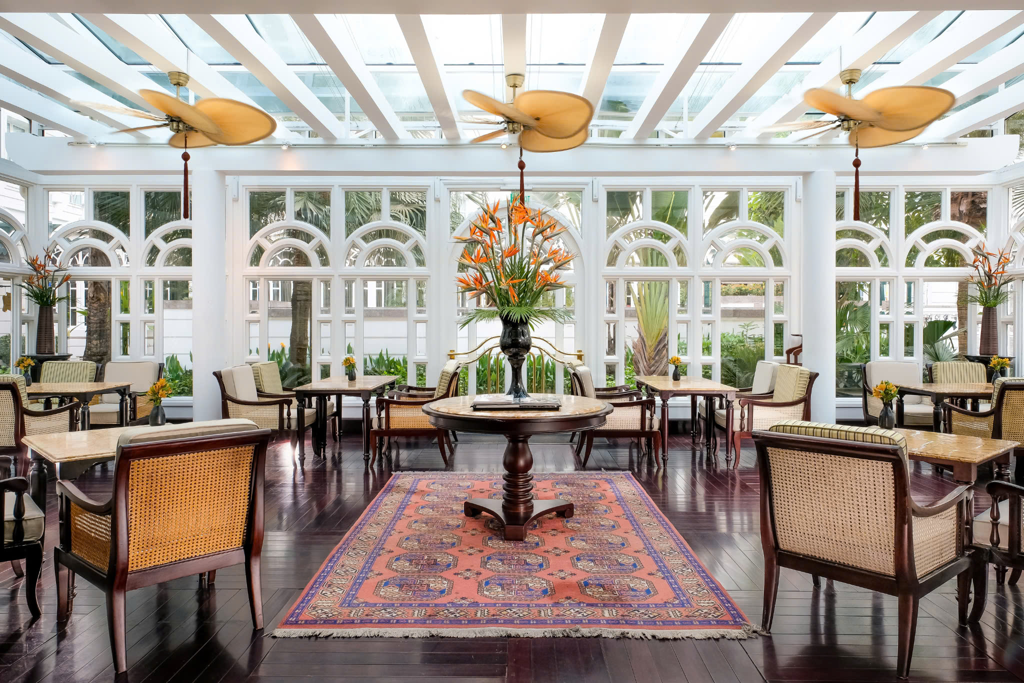 Sunlit dining room with wicker chairs and tiled floor, framed by large windows and ceiling fans under soft daylight.