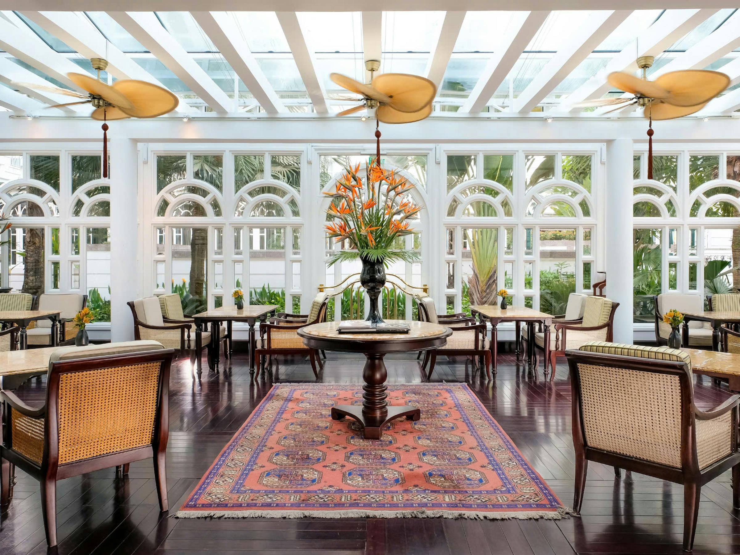 Sunlit dining room with wicker chairs and tiled floor, framed by large windows and ceiling fans under soft daylight.