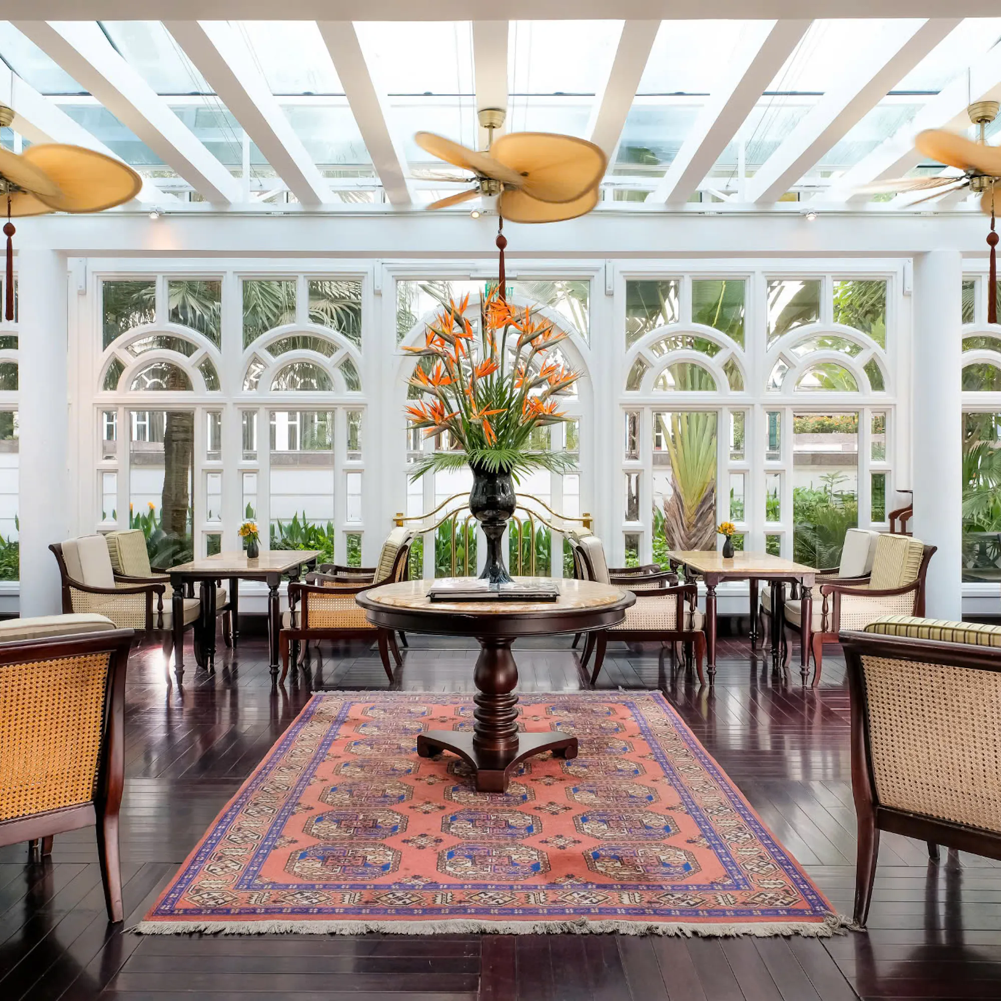 Sunlit dining room with wicker chairs and tiled floor, framed by large windows and ceiling fans under soft daylight.