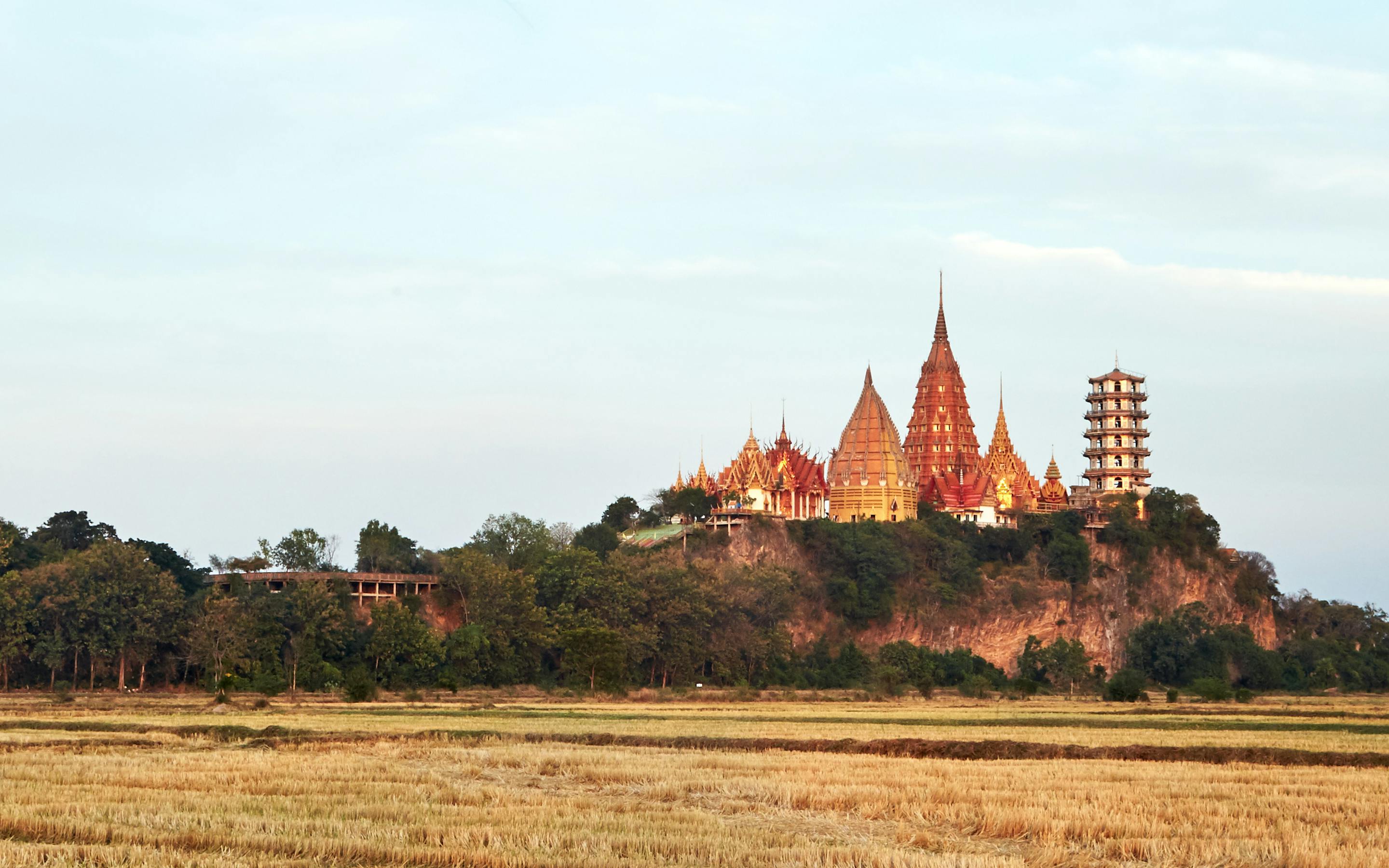 Temple complex rises beyond open fields, with a wide sky and distant trees under soft afternoon light under soft daylight.
