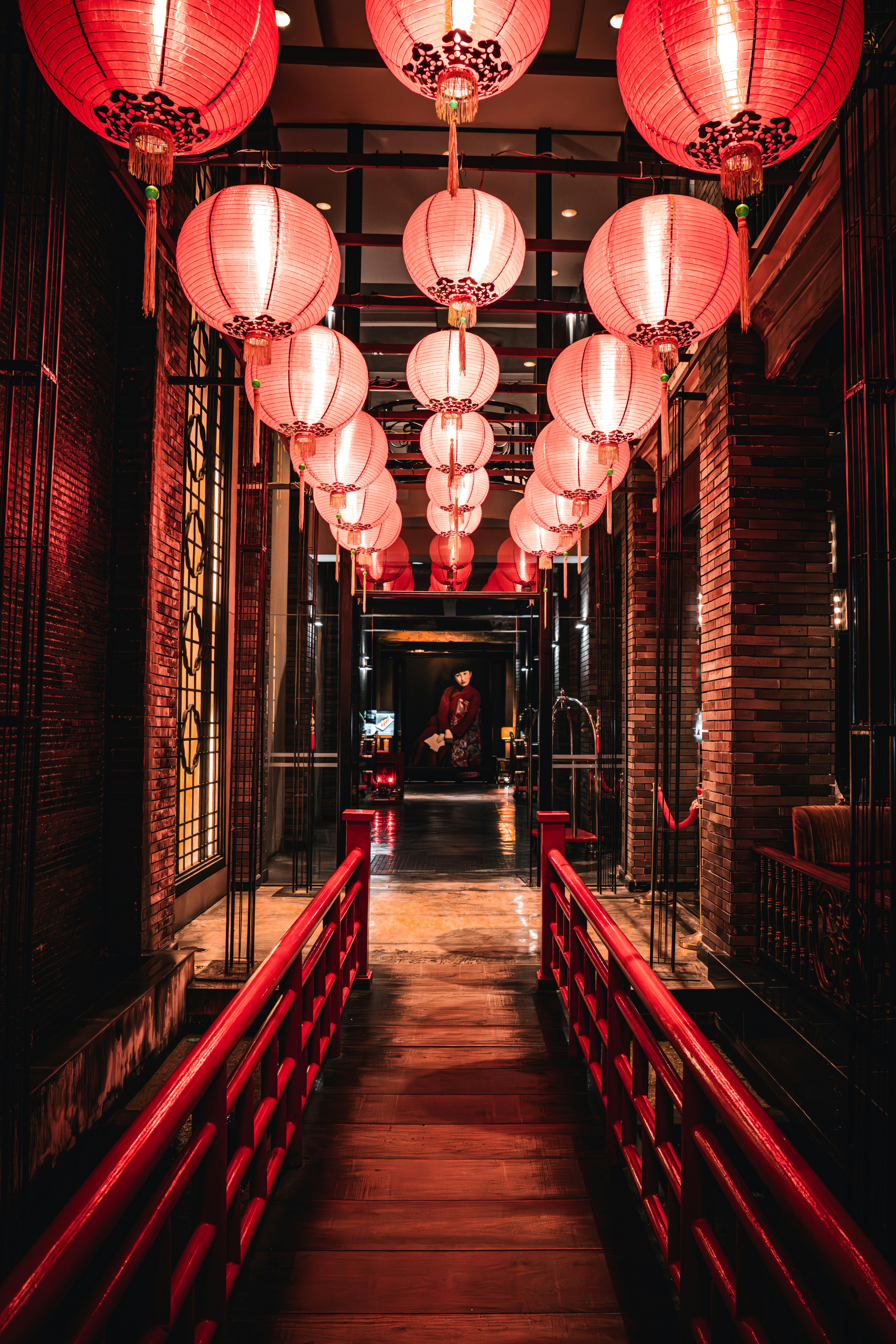 Red lanterns hang over a narrow corridor, with glowing lights and repeating patterns leading into the distance.