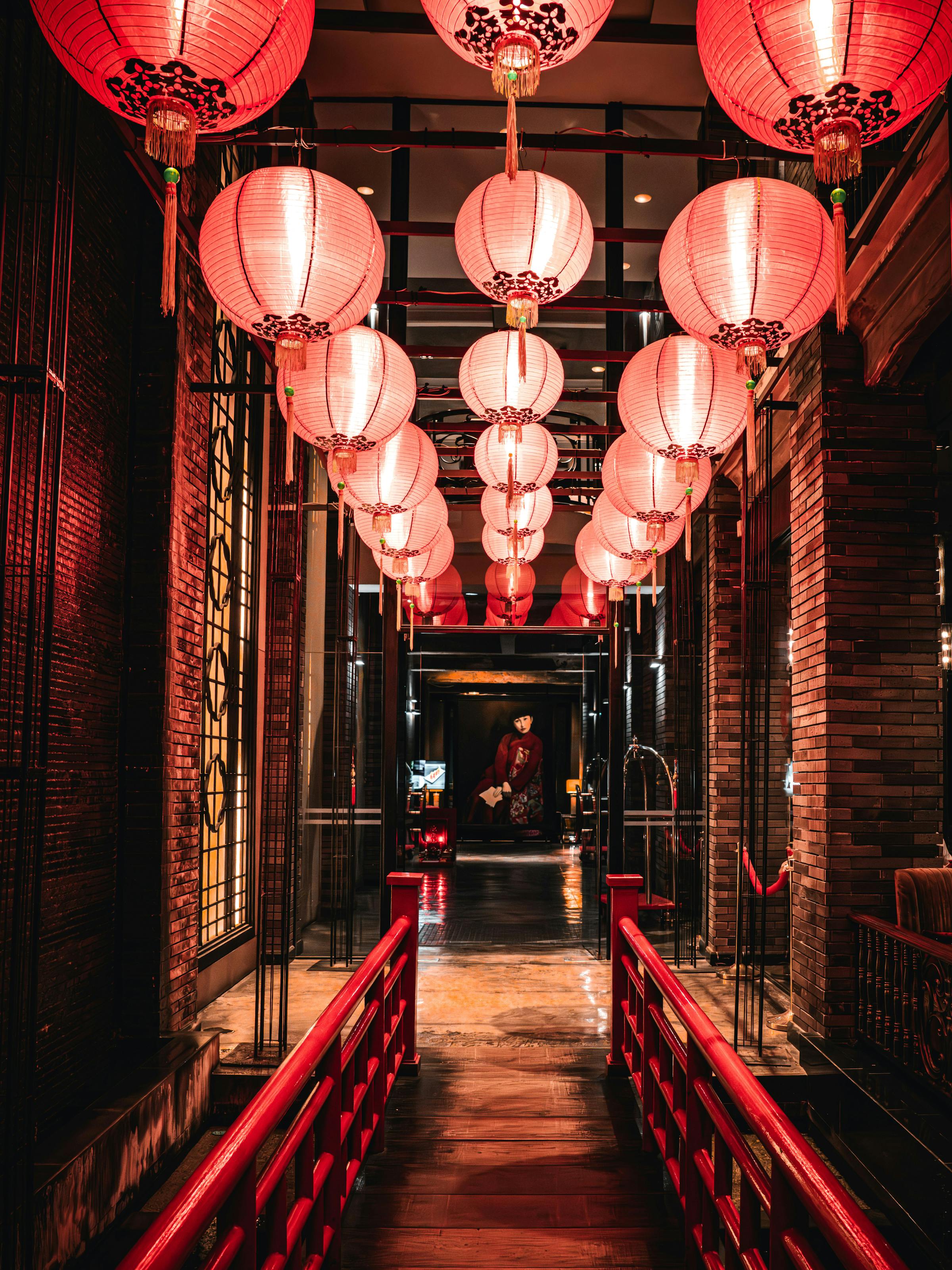Red lanterns hang over a narrow corridor, with glowing lights and repeating patterns leading into the distance.