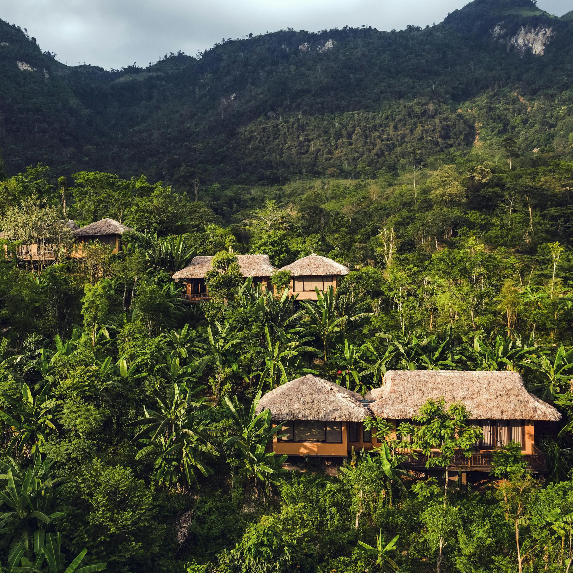 Hillside villas sit above a green valley, with layered mountains and low clouds in the background under soft daylight.