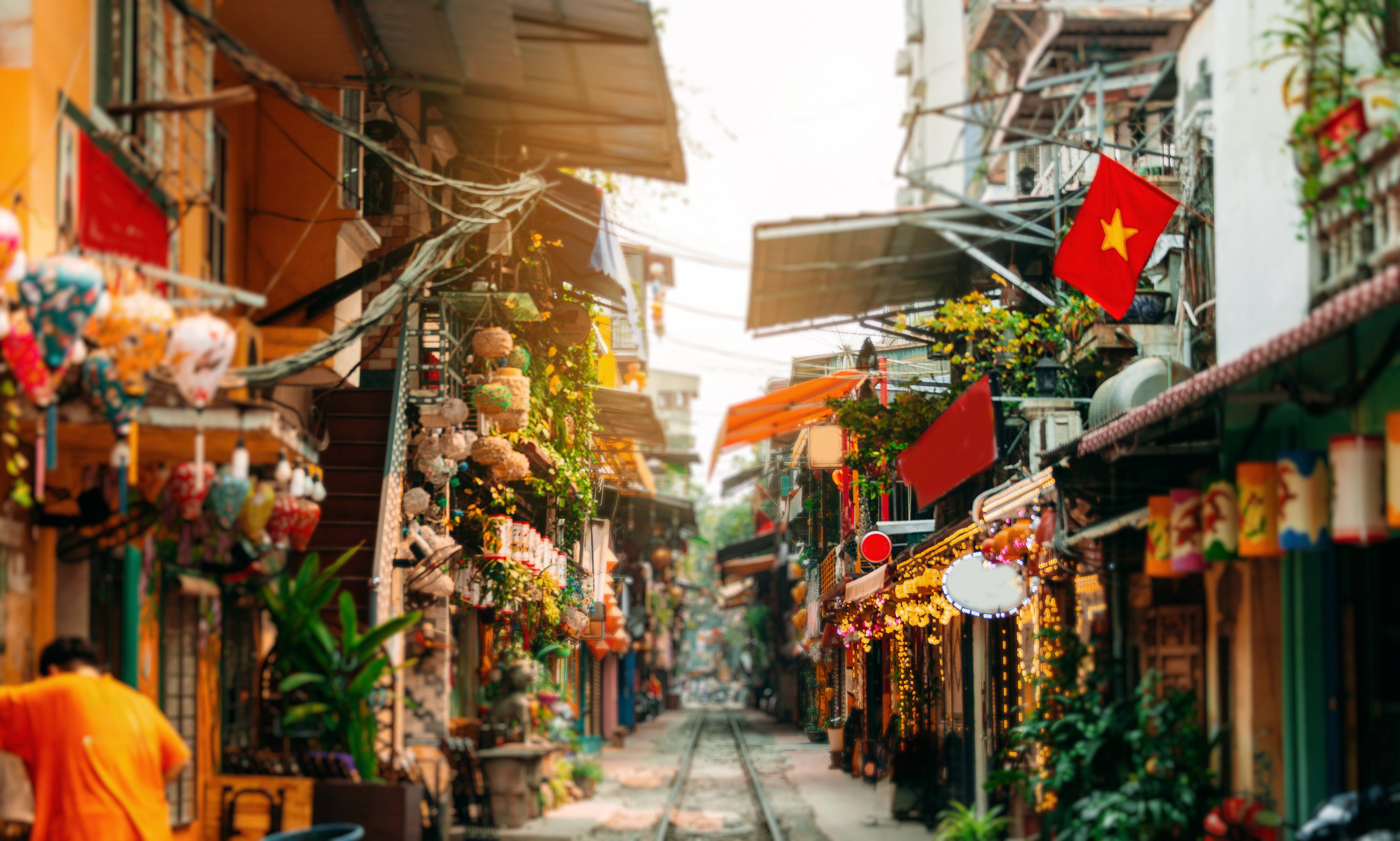 Narrow street lined with shopfronts and hanging lanterns, with flags and warm light spilling into the lane.