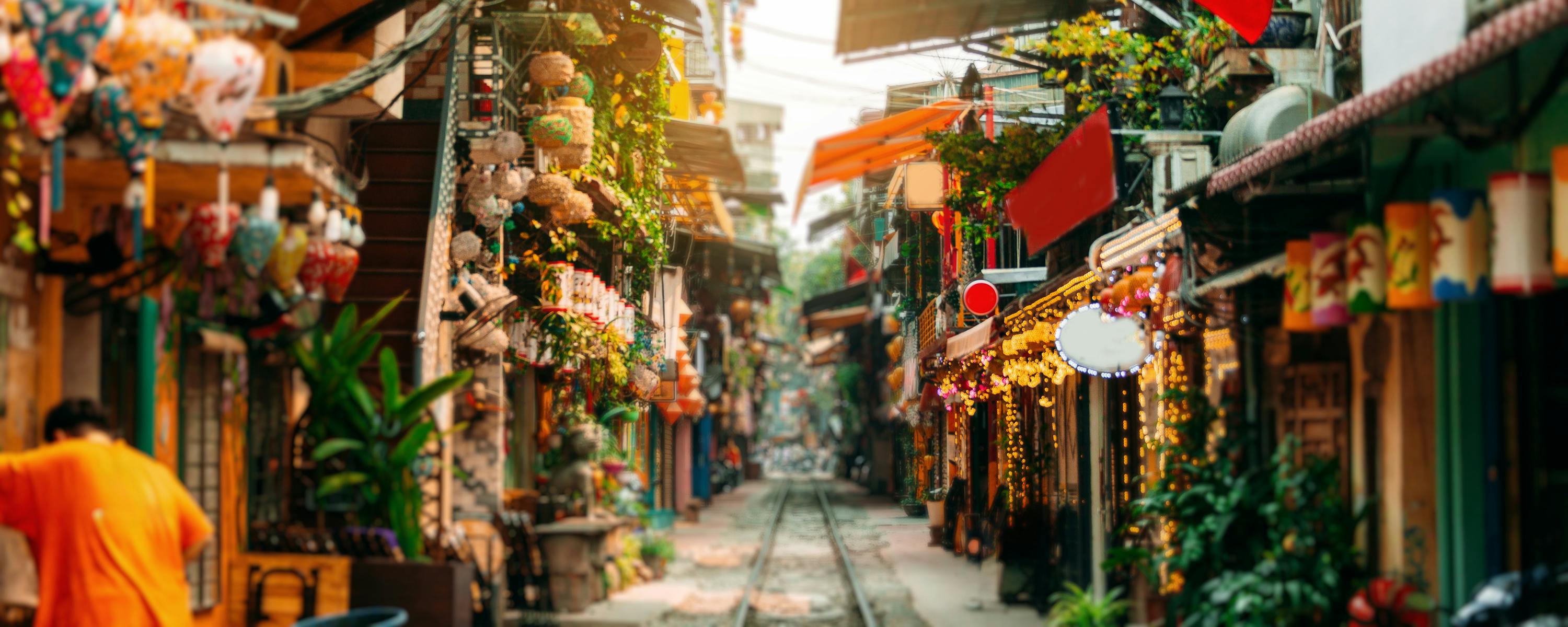 Narrow street lined with shopfronts and hanging lanterns, with flags and warm light spilling into the lane.