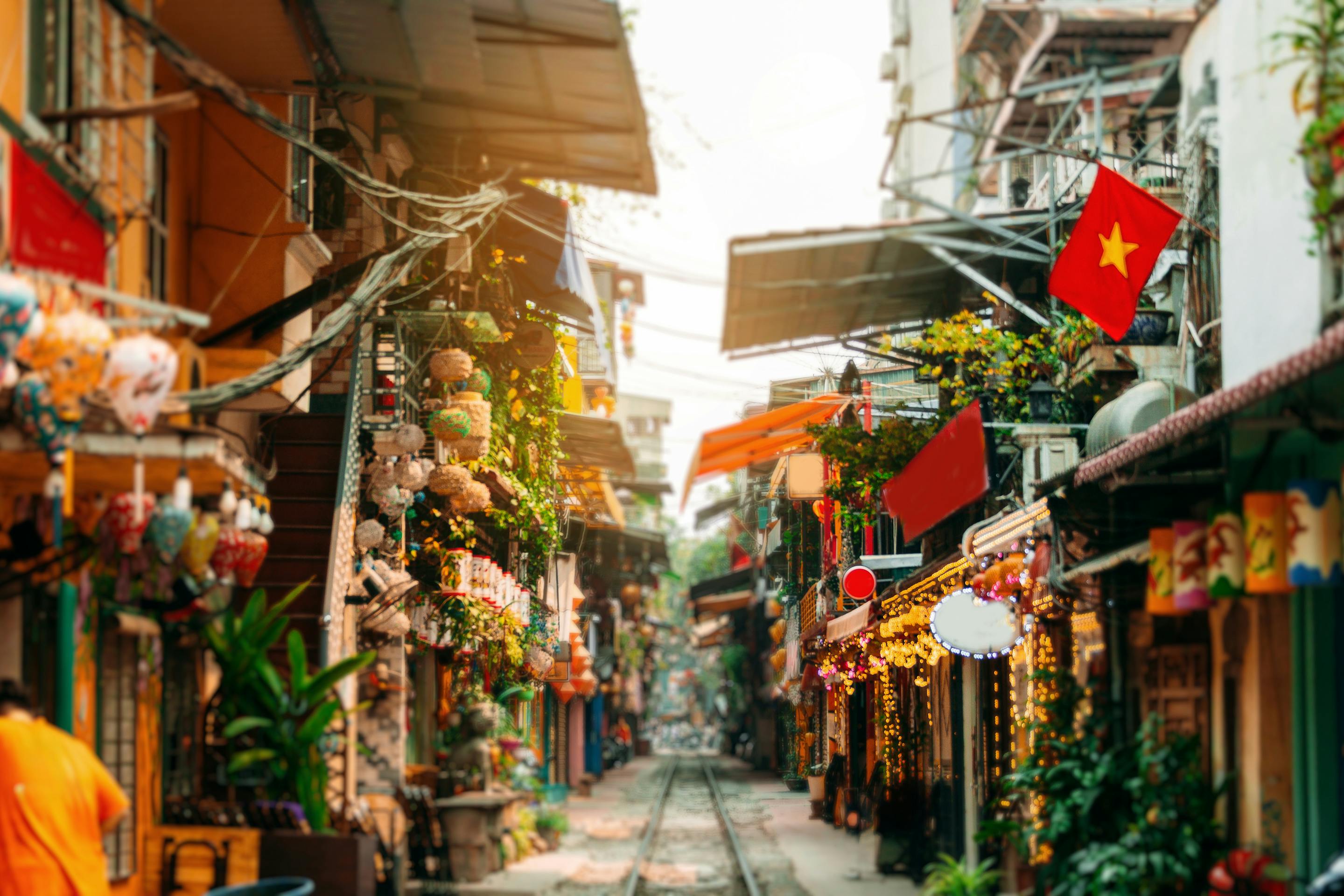 Narrow street lined with shopfronts and hanging lanterns, with flags and warm light spilling into the lane.