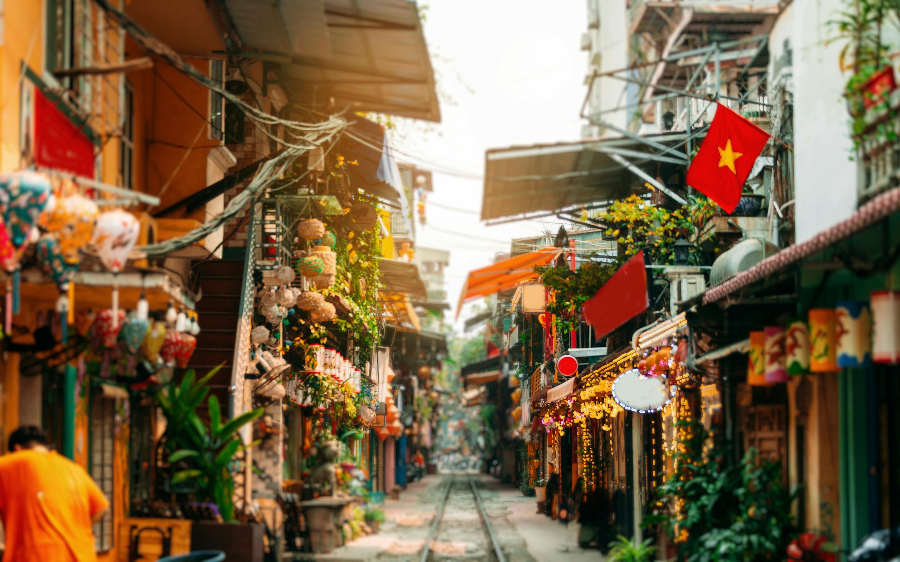 Narrow street lined with shopfronts and hanging lanterns, with flags and warm light spilling into the lane.