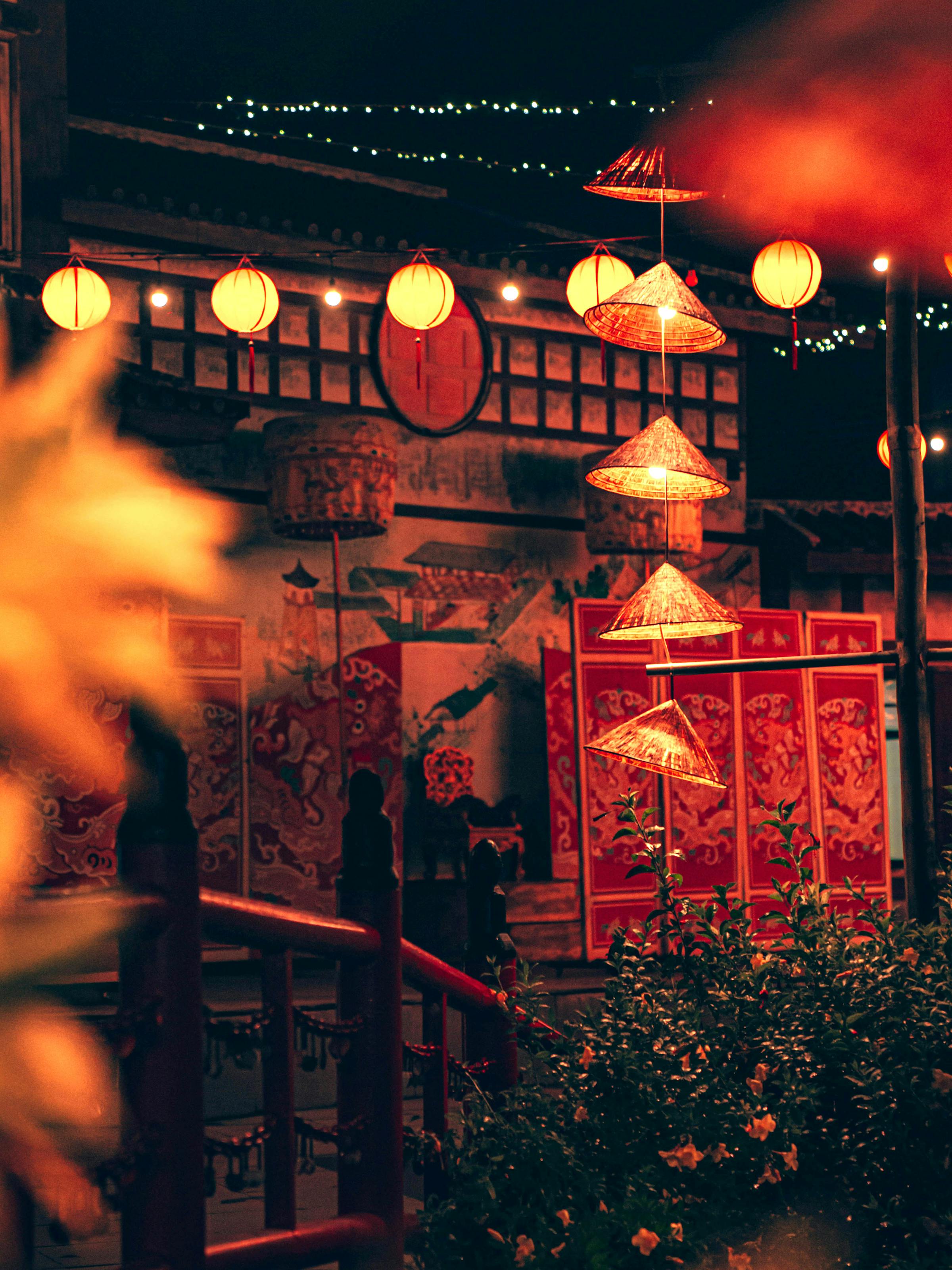 Lantern-lit restaurant scene at night, with glowing lights, wooden beams, and diners seated inside under soft daylight.