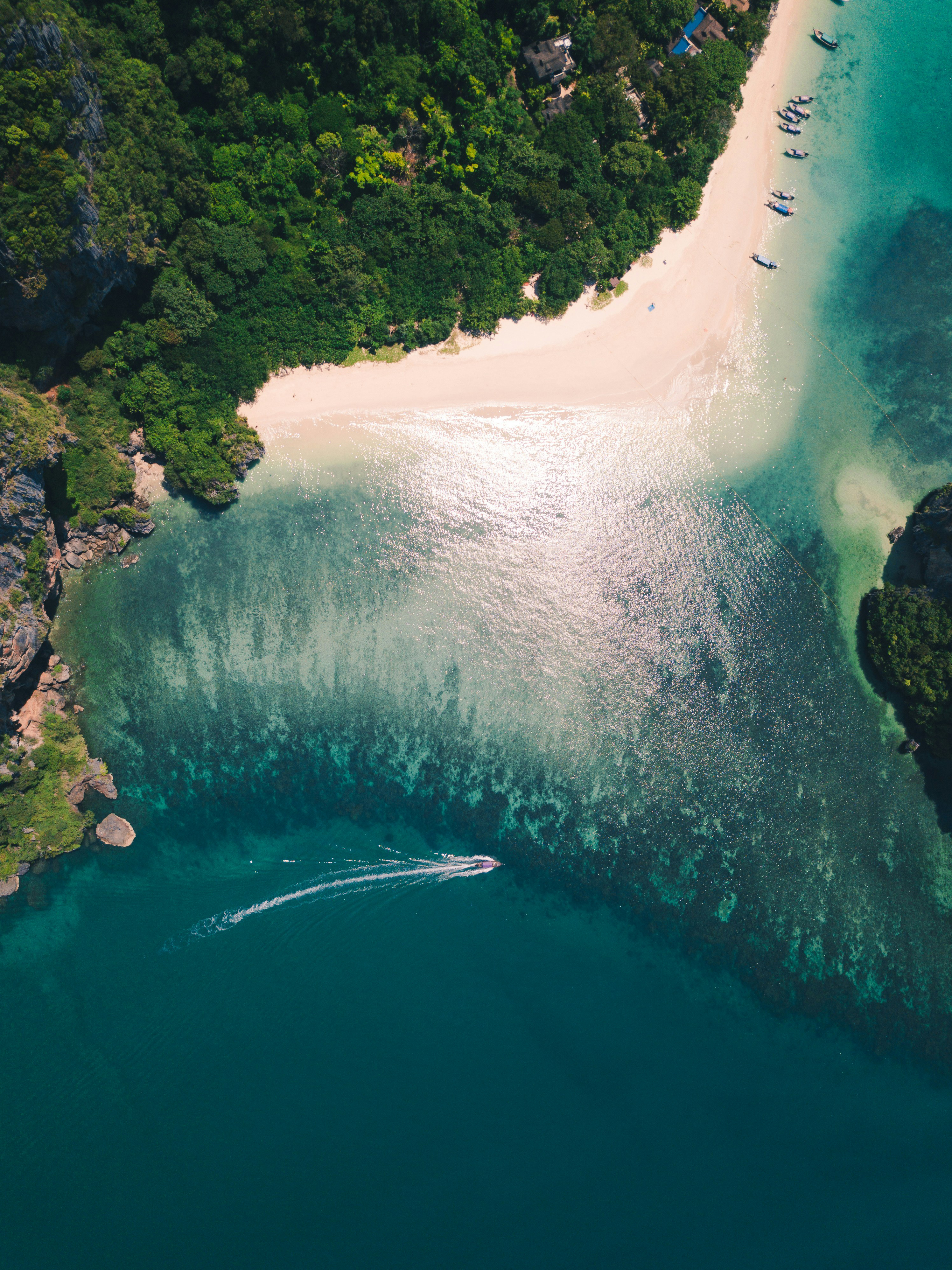 Aerial view of white-sand beach and turquoise lagoon, with dark reef patterns and lush shoreline curves under soft daylight.