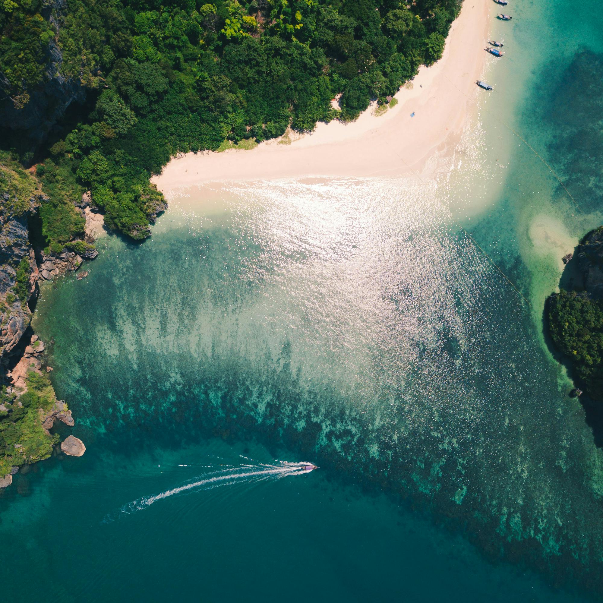 Aerial view of white-sand beach and turquoise lagoon, with dark reef patterns and lush shoreline curves under soft daylight.