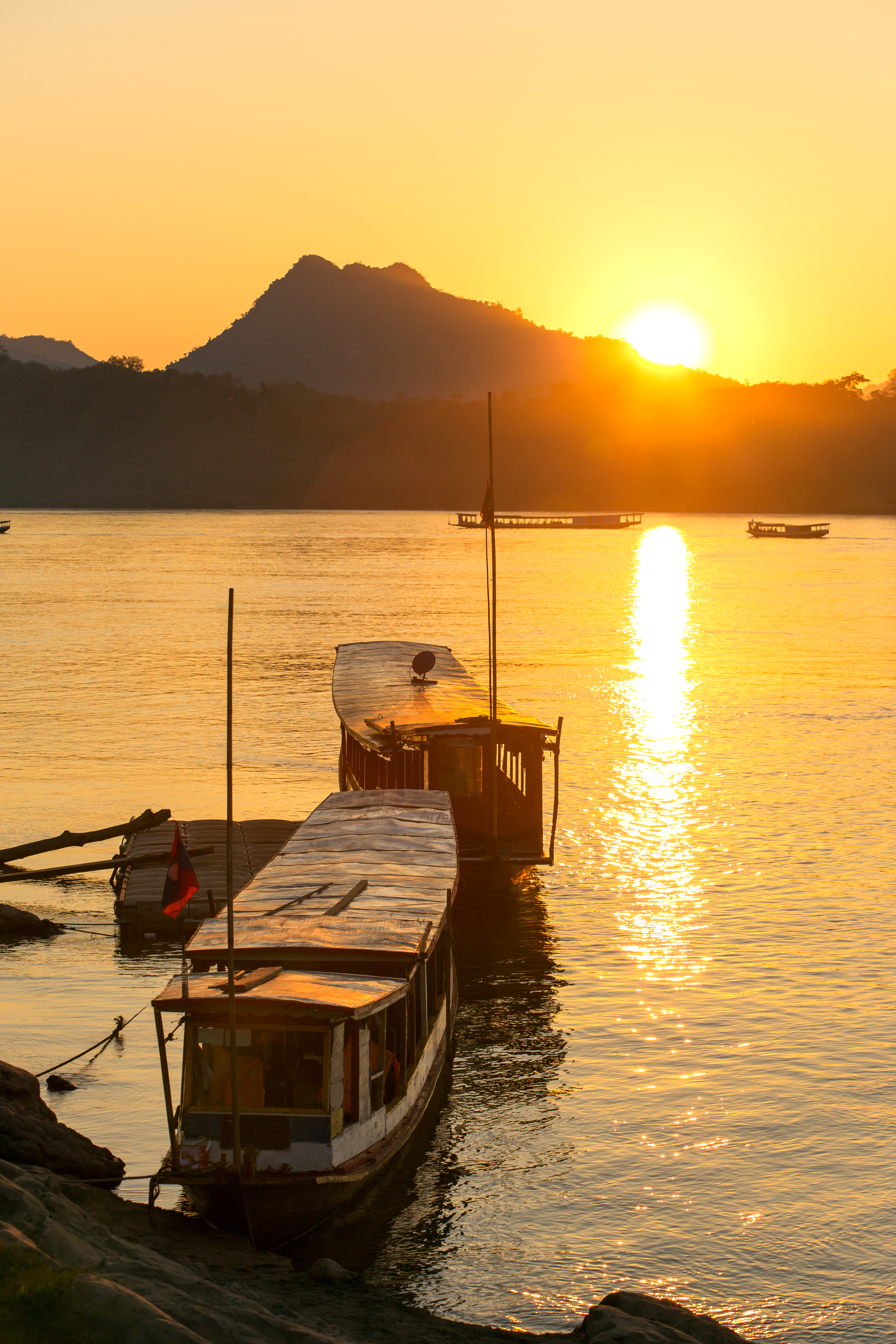 Wooden boat sits at a riverside dock at sunset, with golden light reflecting across calm water at sunset